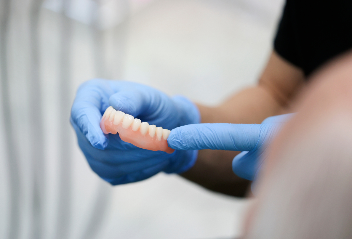 A person wearing blue gloves is holding a denture in their hands.