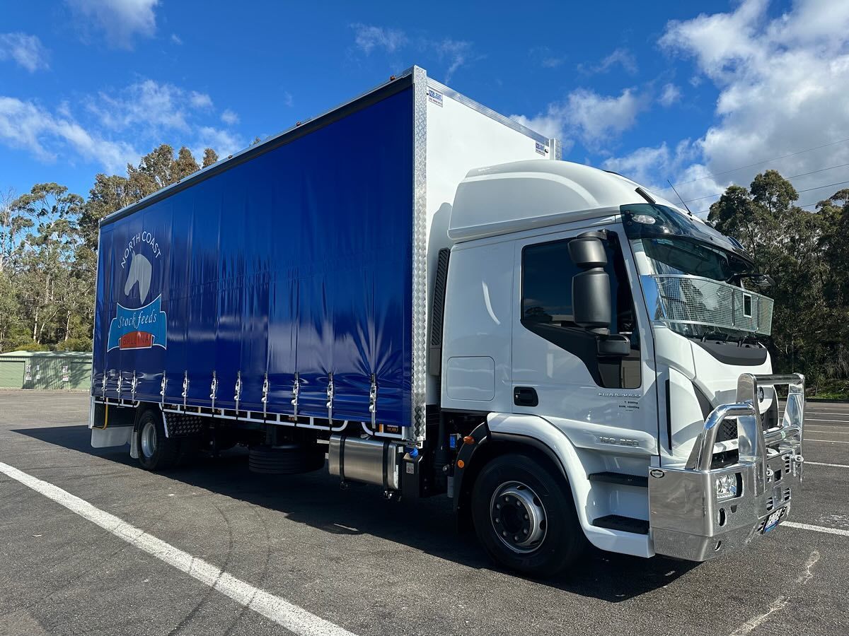 White and Blue Truck With Tarp Sides Parked on Asphalt — North Coast Stock Feeds in Woodburn, NSW