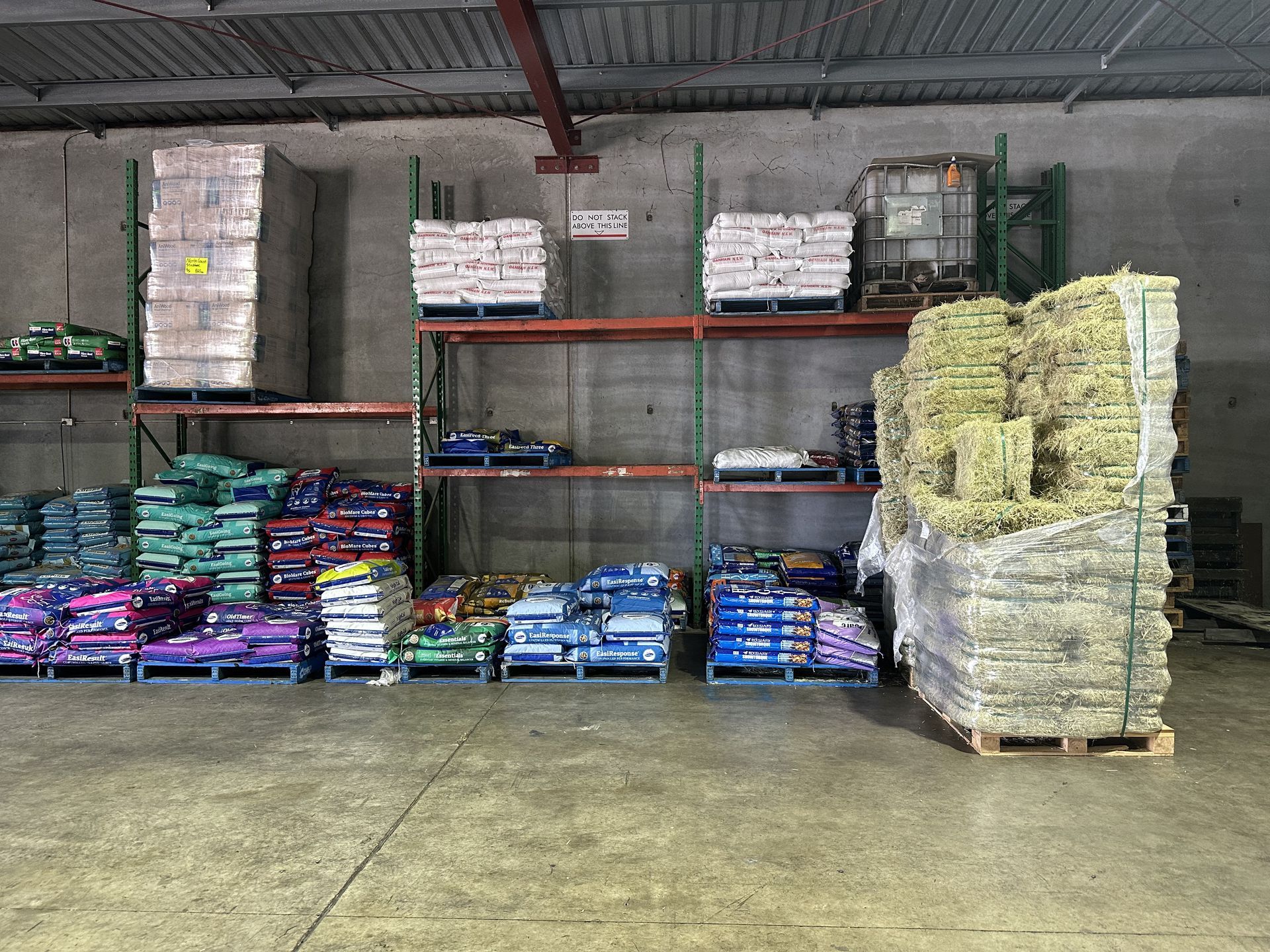 Warehouse interior, shelves stocked with bags and hay bales on pallets. Gray concrete floor. — North Coast Stock Feeds in Wardell, NSW