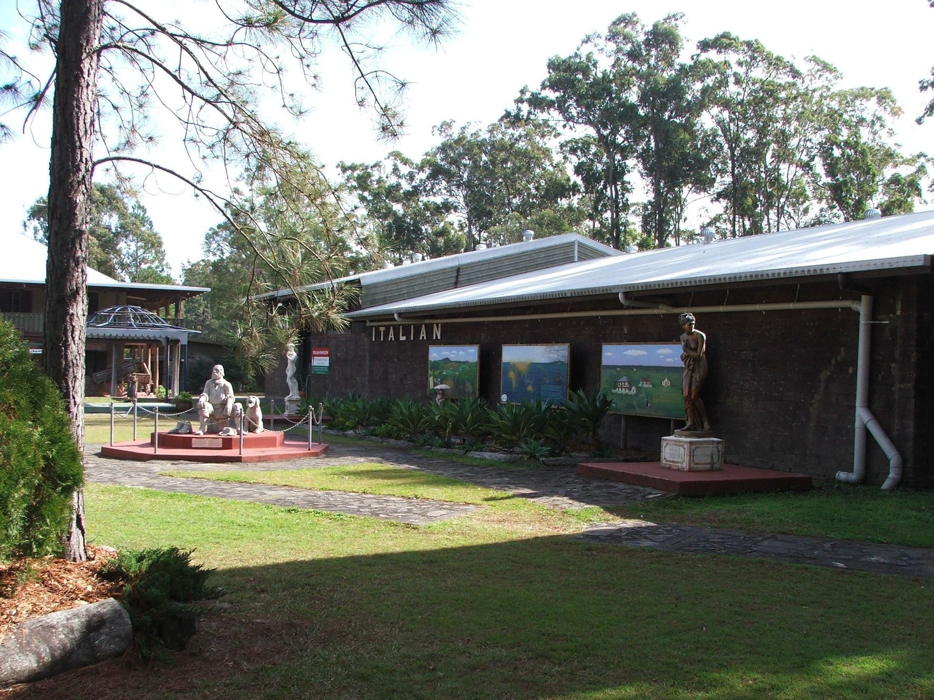 Exterior view of a museum with statues and informational displays on the lawn. Wooden buildings under blue sky. — North Coast Stock Feeds in Wardell, NSW