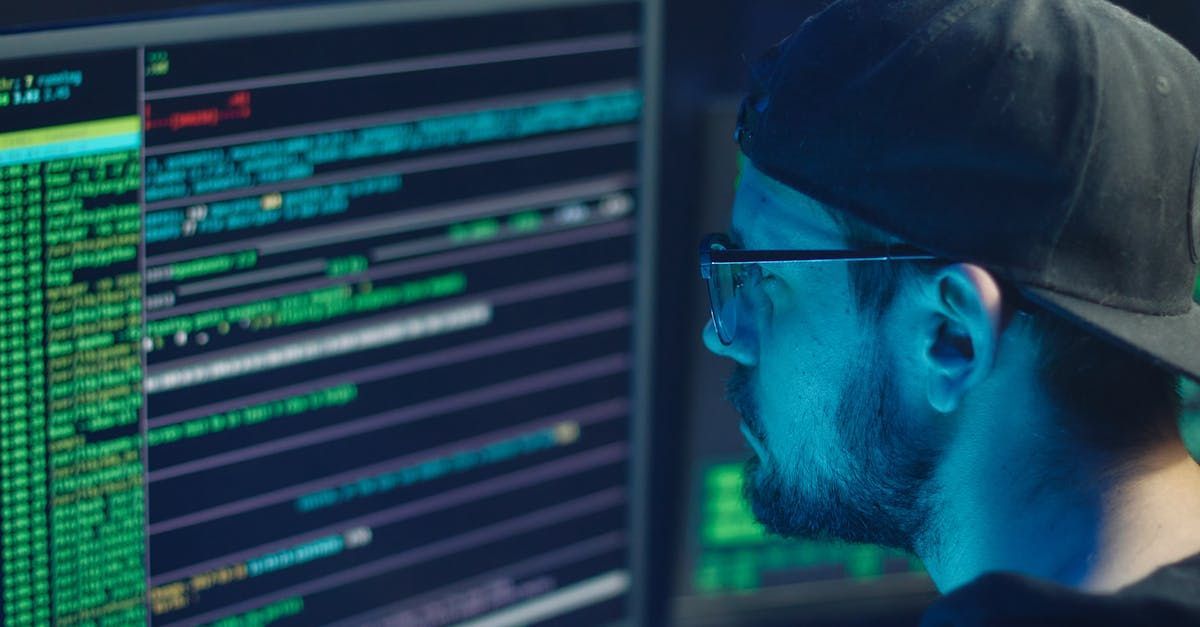 A man wearing a hat and glasses is looking at a computer screen.