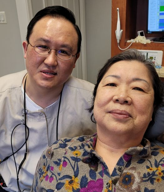 Dentist and patient smiling together in a dental office. The dentist wears glasses and scrubs.