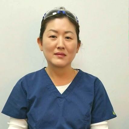 Esther wearing a blue scrub top and protection glasses and looking at the camera .