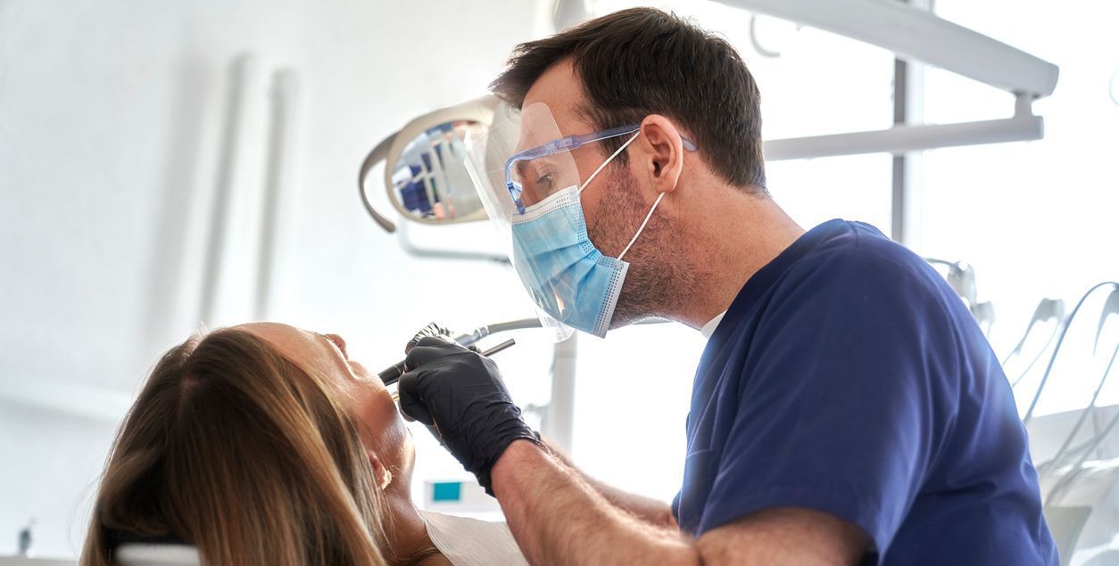 A dentist is examining a woman 's teeth in a dental office.