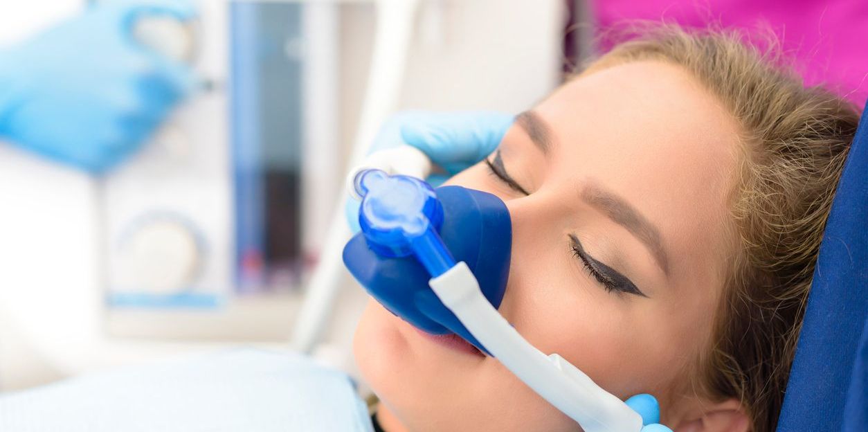 A woman is laying in a dental chair with an oxygen mask on her face.