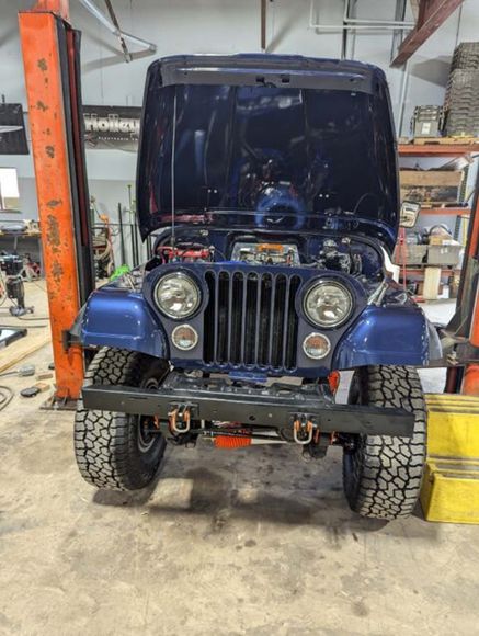 A blue jeep with the hood up is parked in a garage.