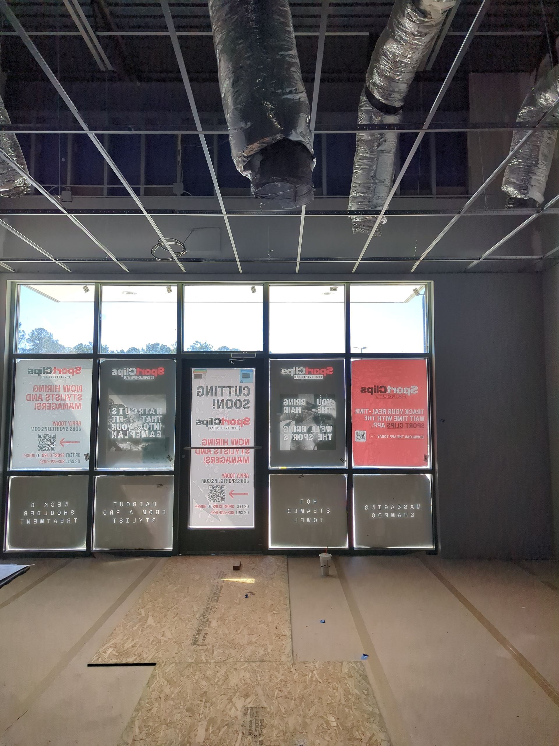 An interior view of a storefront under construction with exposed ceiling ducts and papered windows featuring business ads.