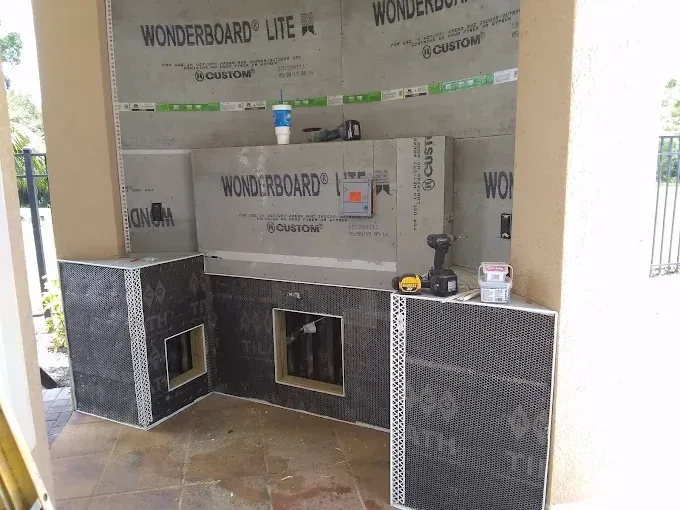 An outdoor kitchen island under construction featuring WonderBoard Lite panels, framing, and tools on a patio.