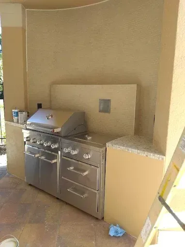 An outdoor kitchen featuring stainless steel built-in grill and drawers, granite countertops, and beige stucco walls.