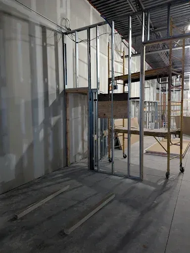 An interior construction site showing metal wall framing, partially installed drywall, and scaffolding.