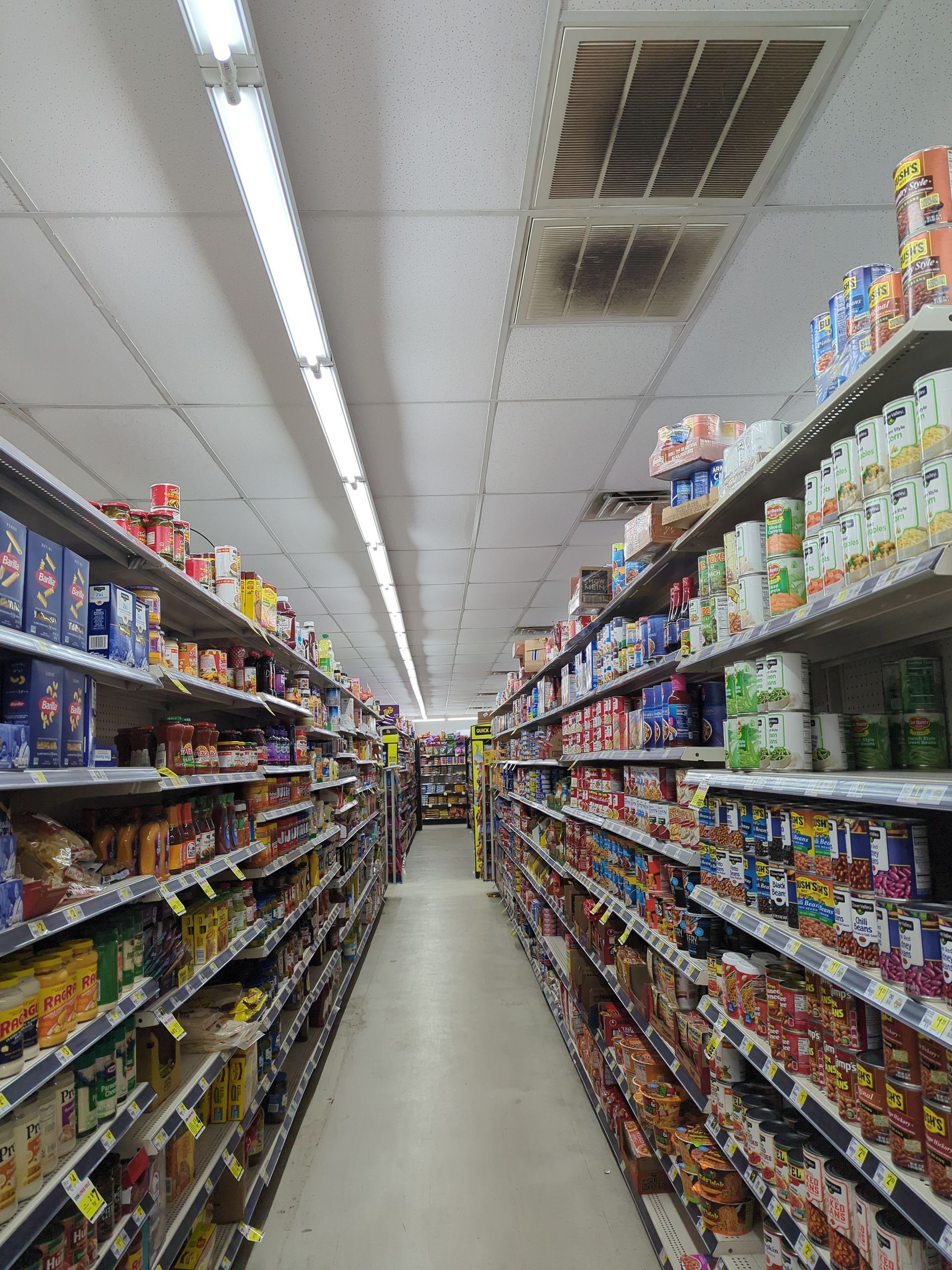 A grocery store aisle with shelves stocked with various packaged food products under bright overhead lighting.