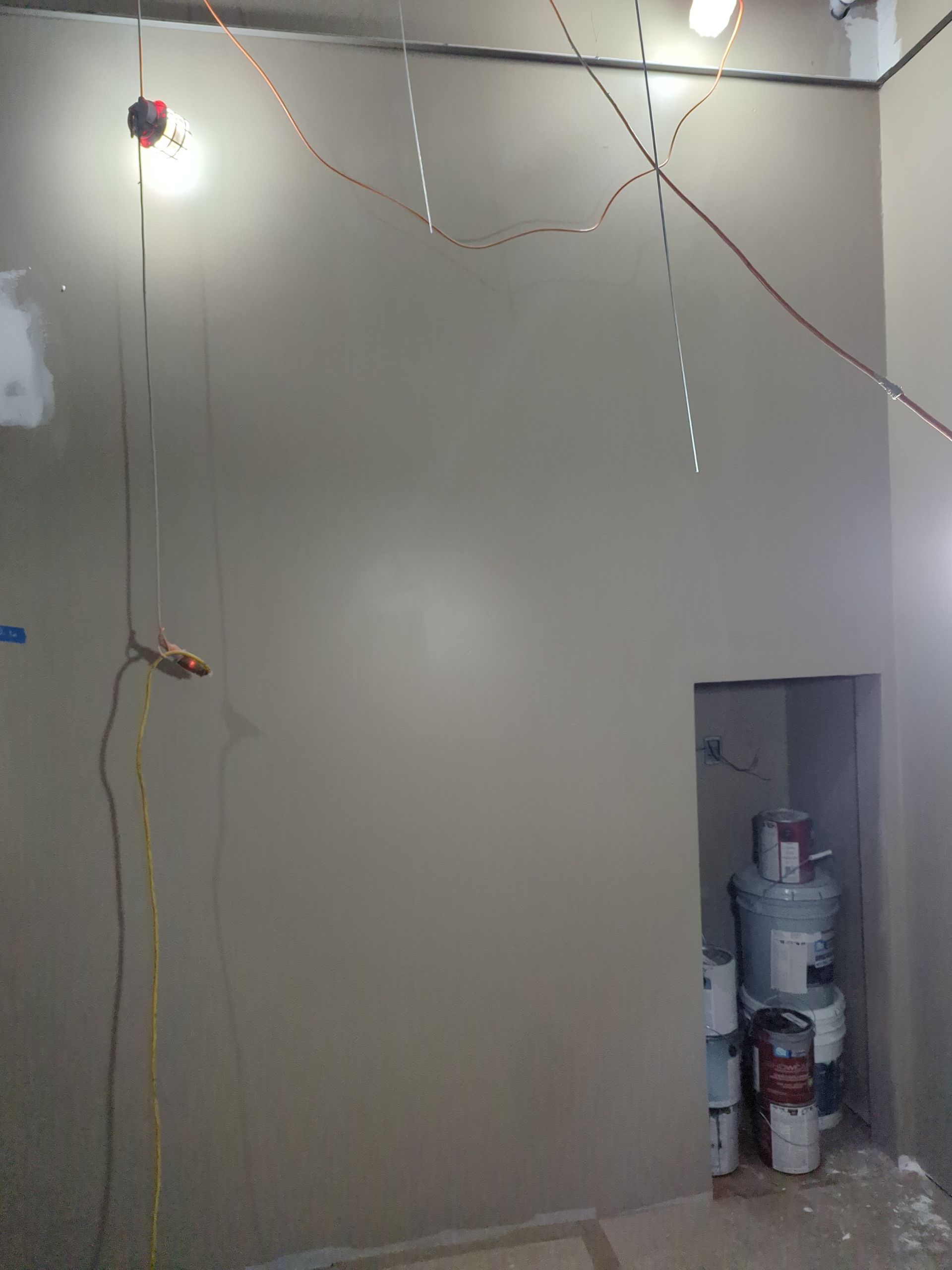 A gray wall in a room under construction, with a hanging light fixture and an alcove containing stacked containers.