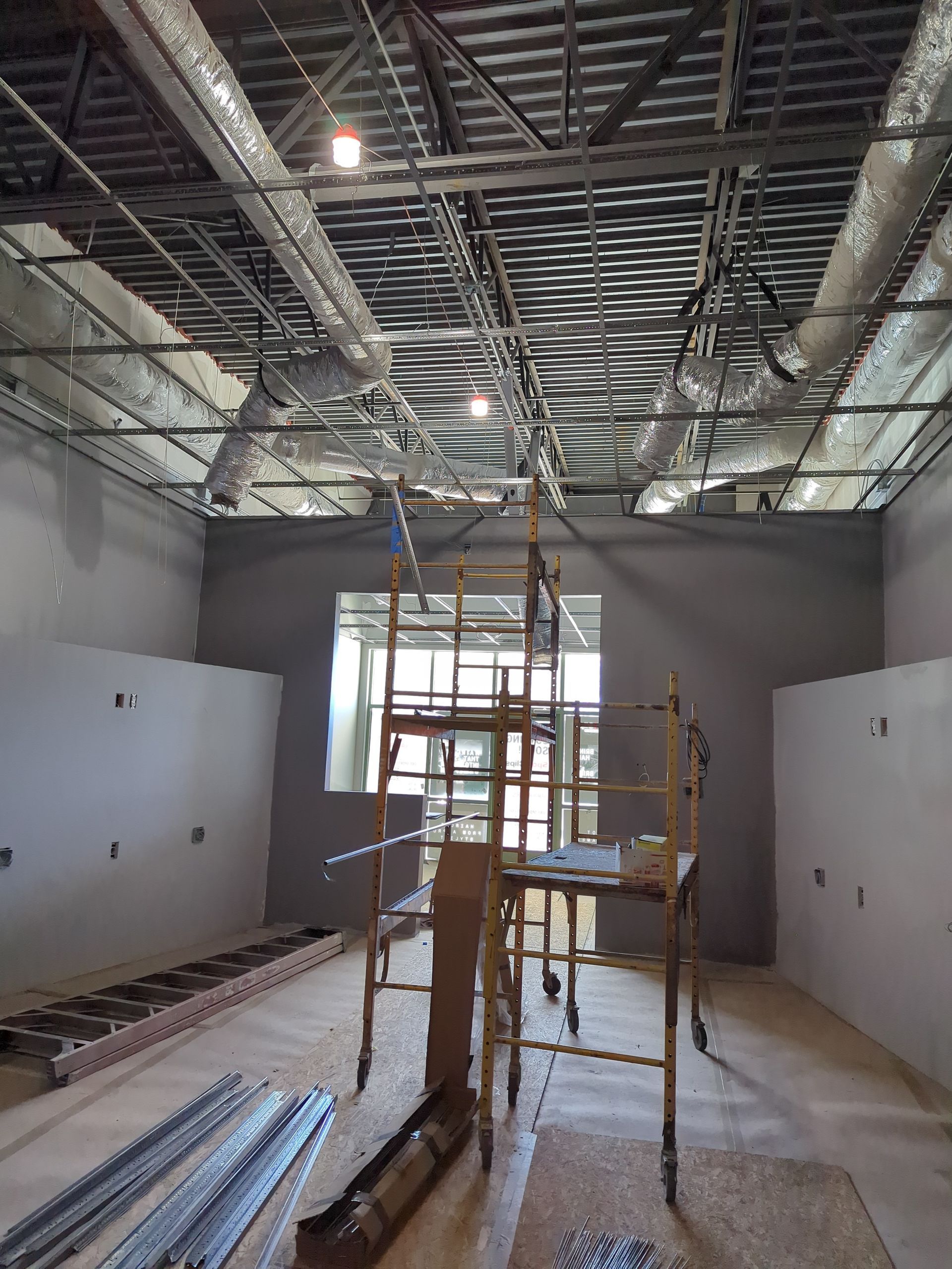 An unfinished interior room with gray walls, exposed ceiling ductwork, a metal scaffolding tower, and construction tools.