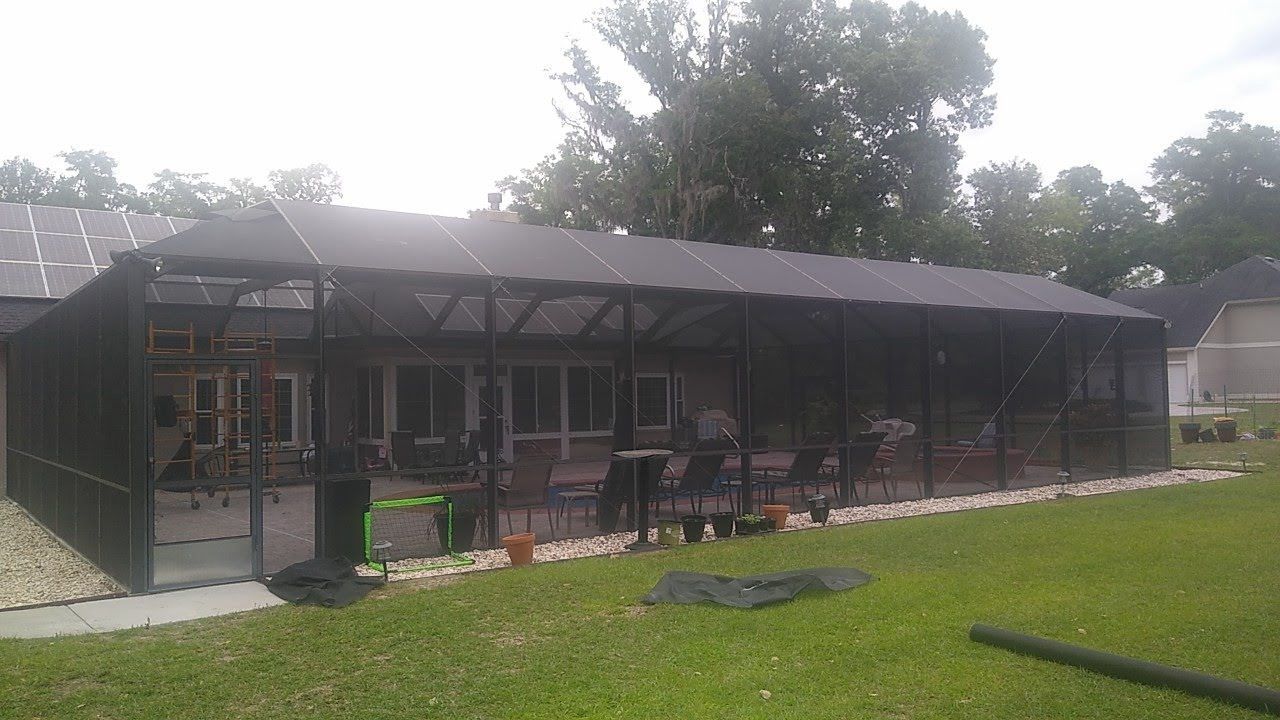 A screened-in patio enclosure attached to a house, featuring a dark frame and mesh walls over a paved outdoor seating area.