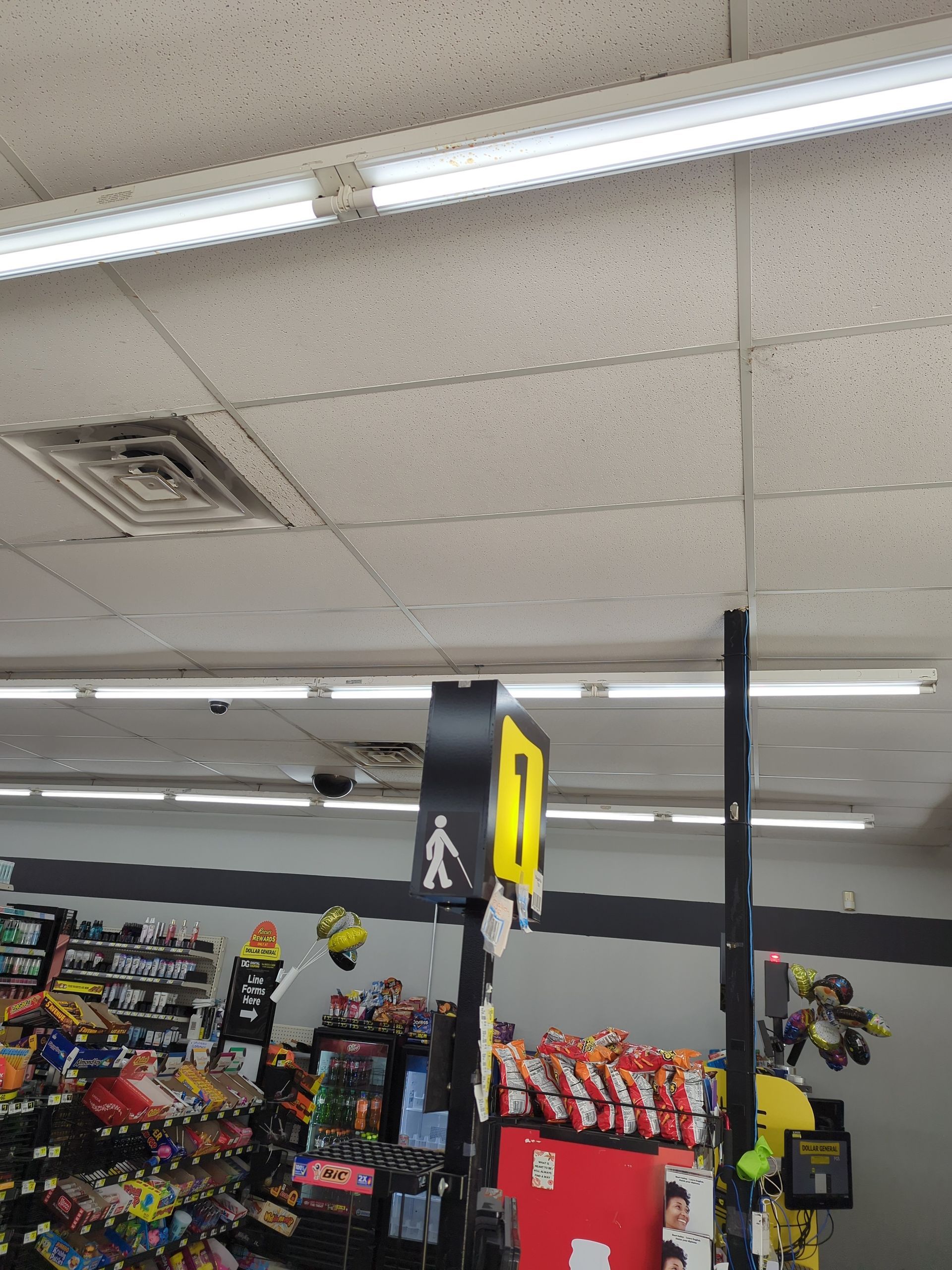 A yellow and black store aisle sign with a walking person icon hangs from the ceiling above merchandise in a retail store.