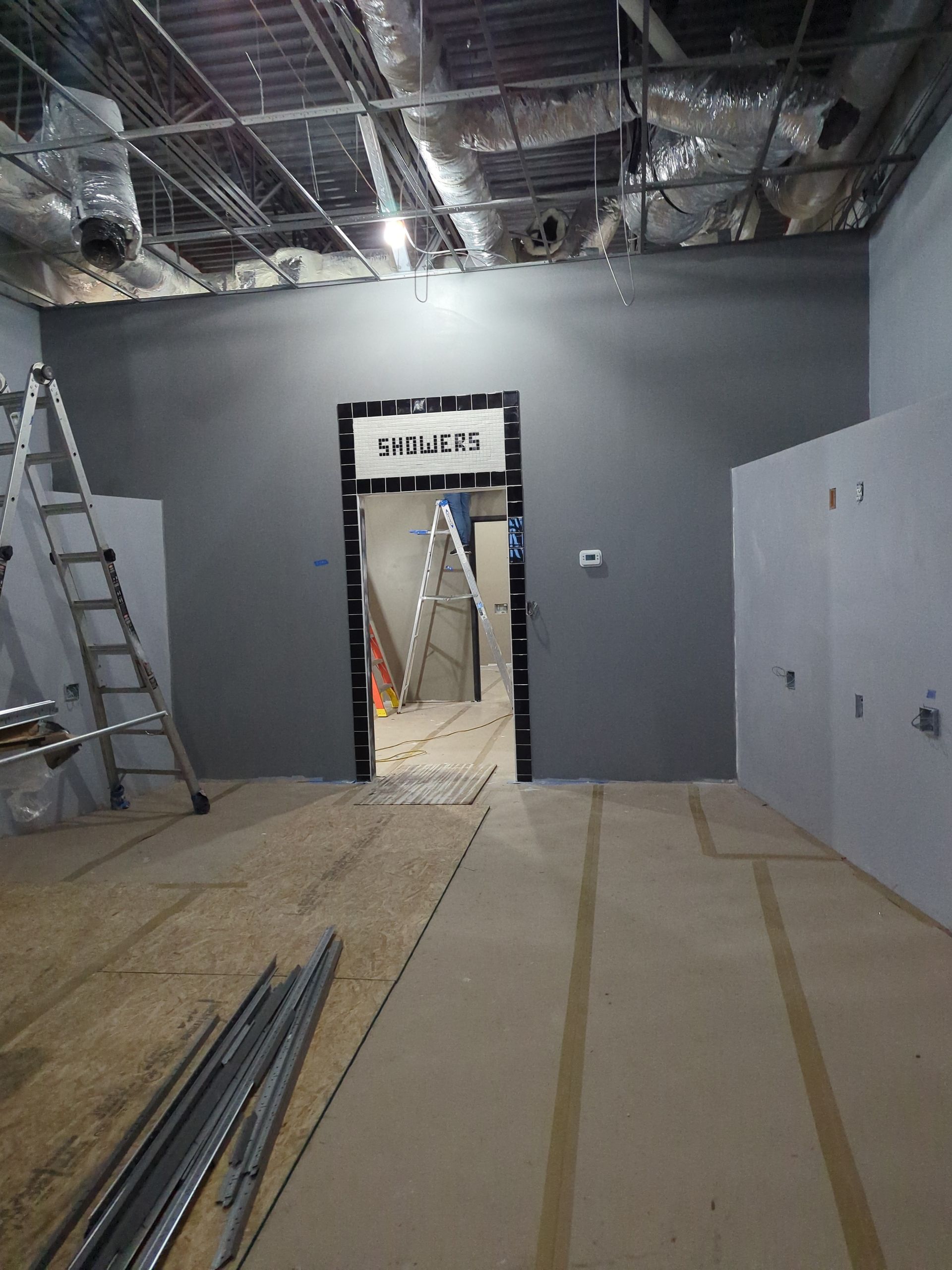 An interior room under construction with gray walls, an open doorway, scaffolding, and floor materials.