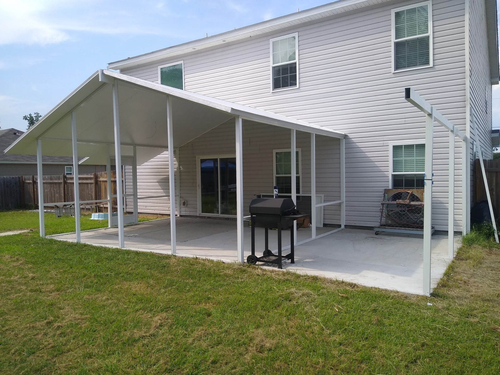 A white two-story house with a covered patio area in the backyard featuring a grill and an unfinished metal frame support.