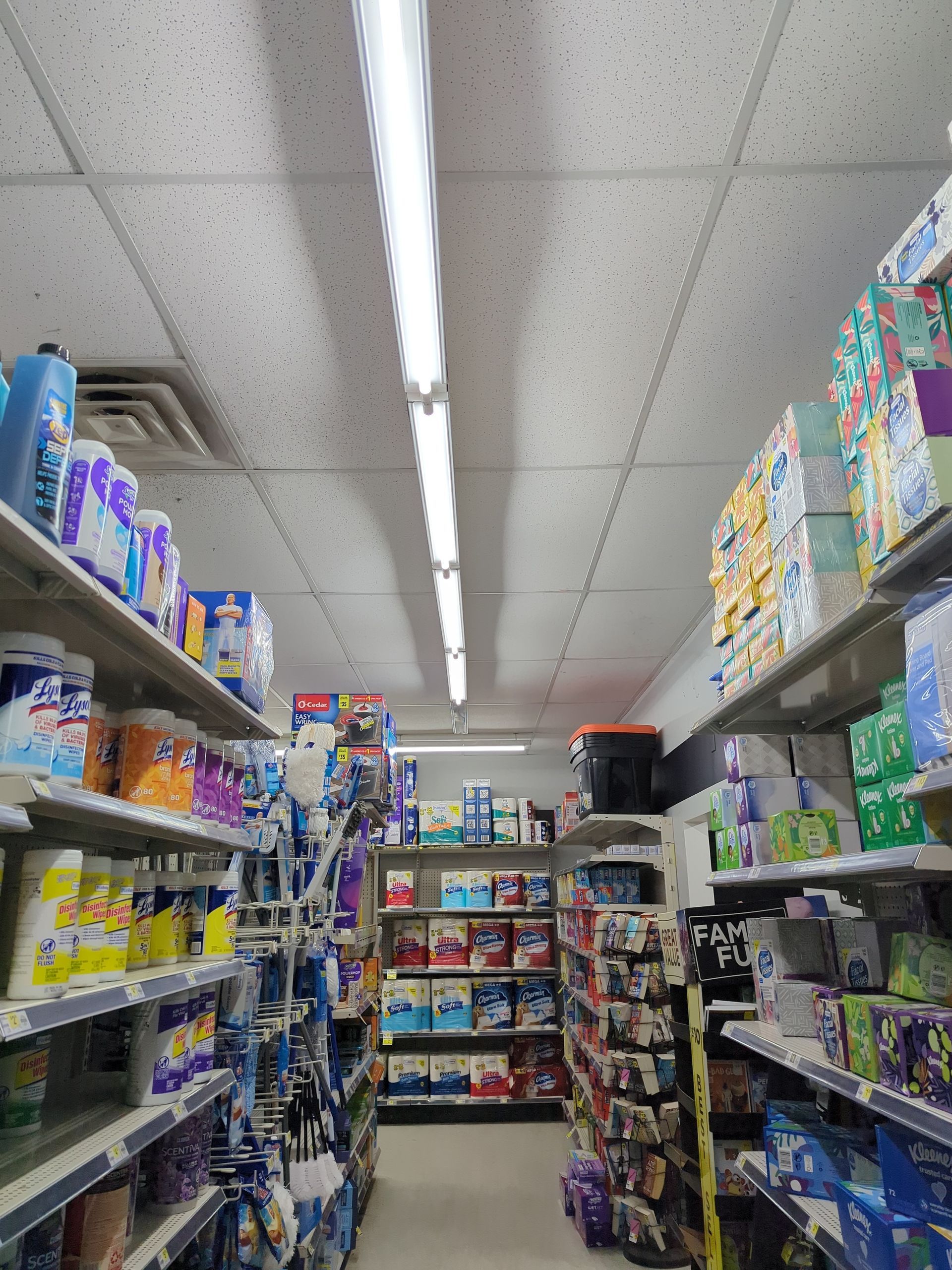 A view down an aisle in a retail store stocked with various cleaning products, paper goods, and household supplies.