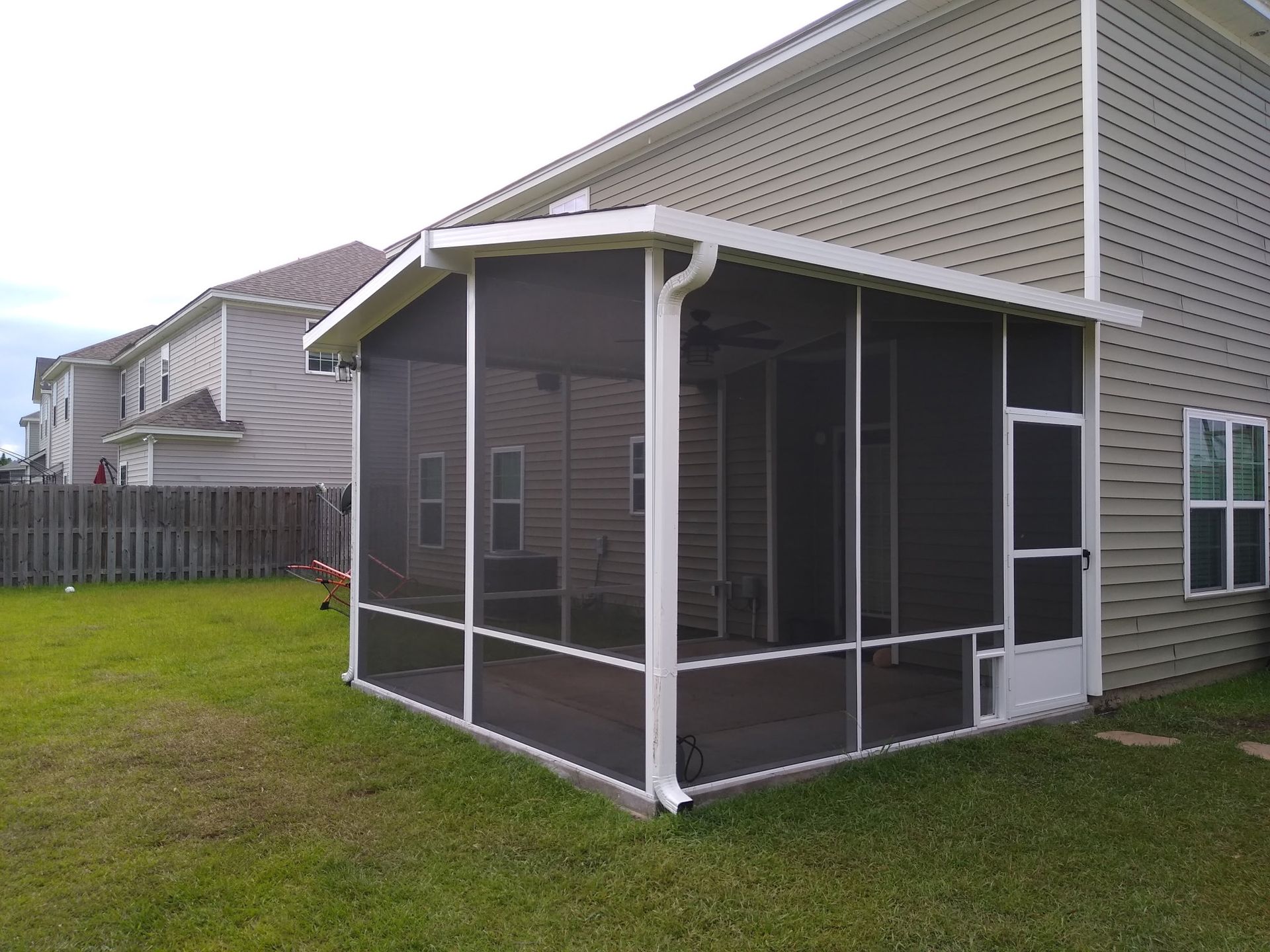 A white-framed screened-in porch attached to the back of a tan, two-story suburban house with a green lawn.