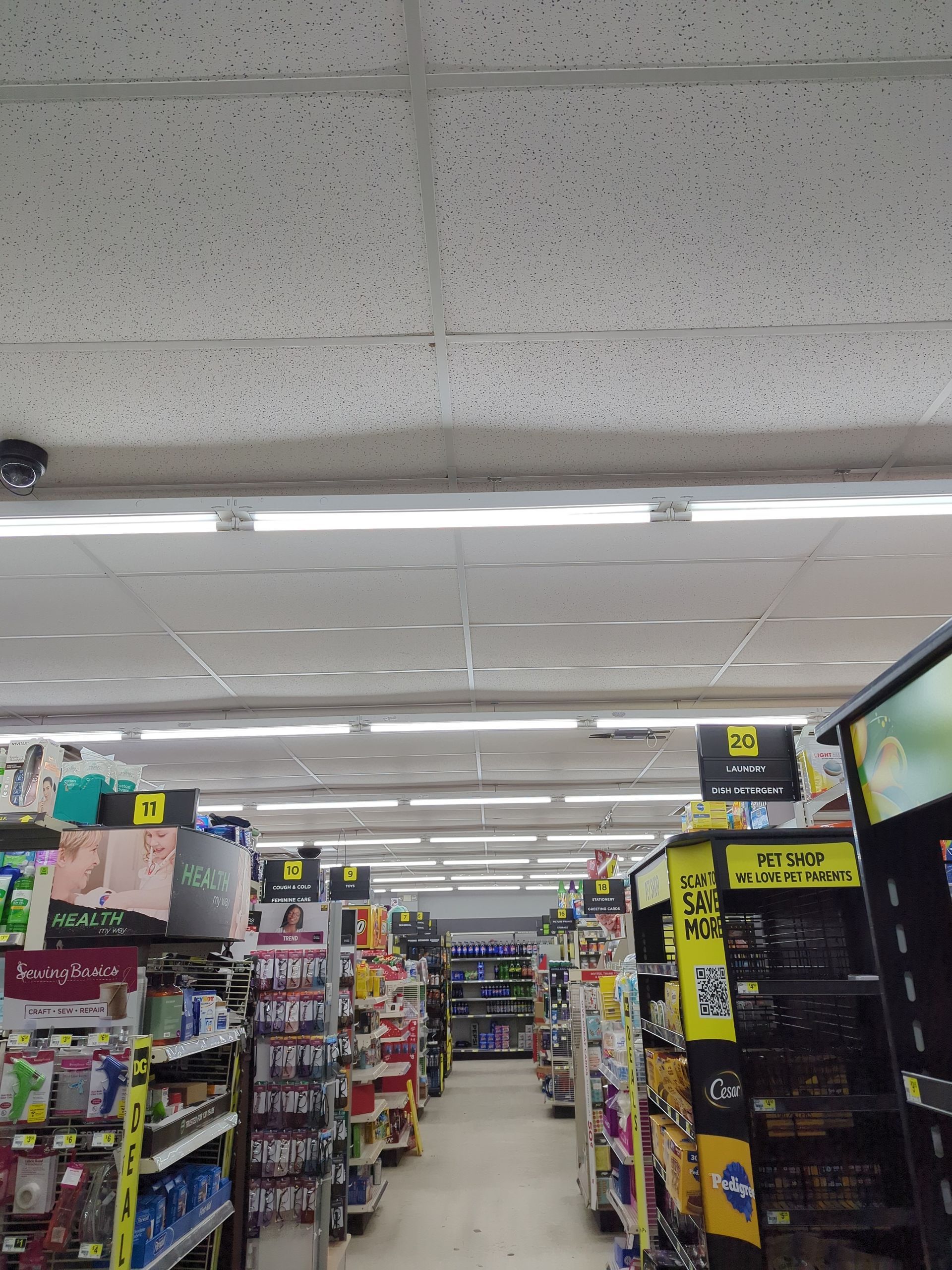 A view down an aisle in a convenience store, lined with shelves filled with various products and fluorescent lighting.