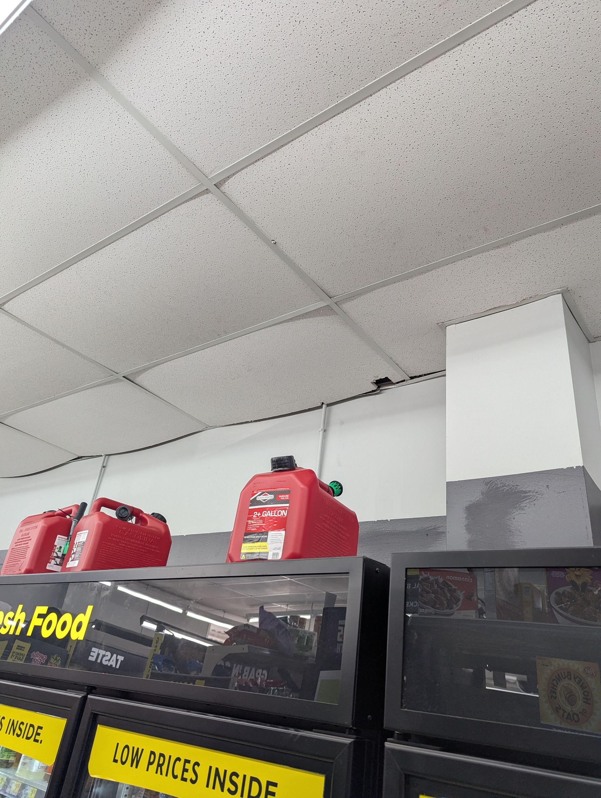 Two red gasoline cans sitting on top of a convenience store refrigerated display case.
