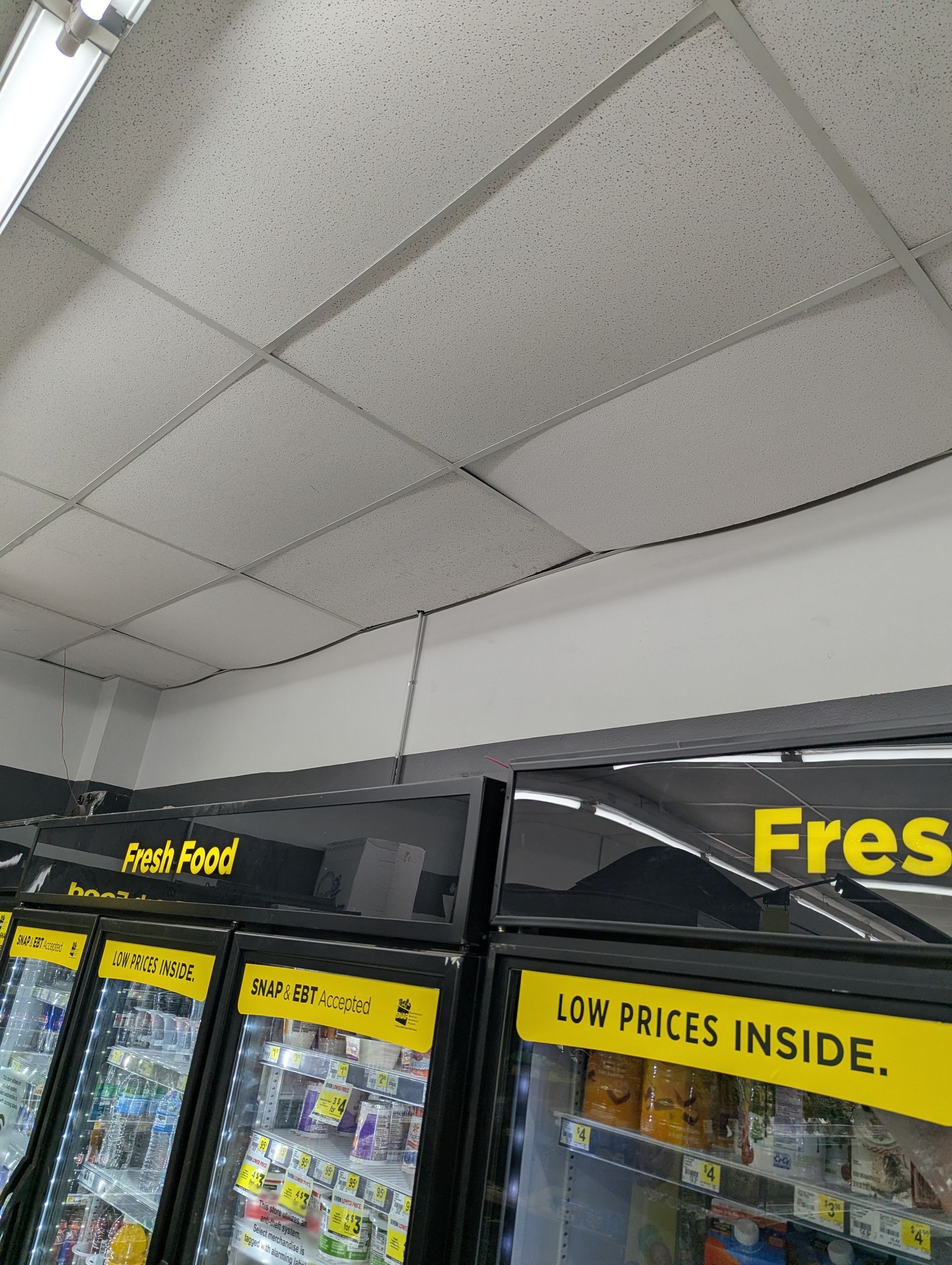 A drop ceiling above refrigerated grocery display cases with yellow signs reading 