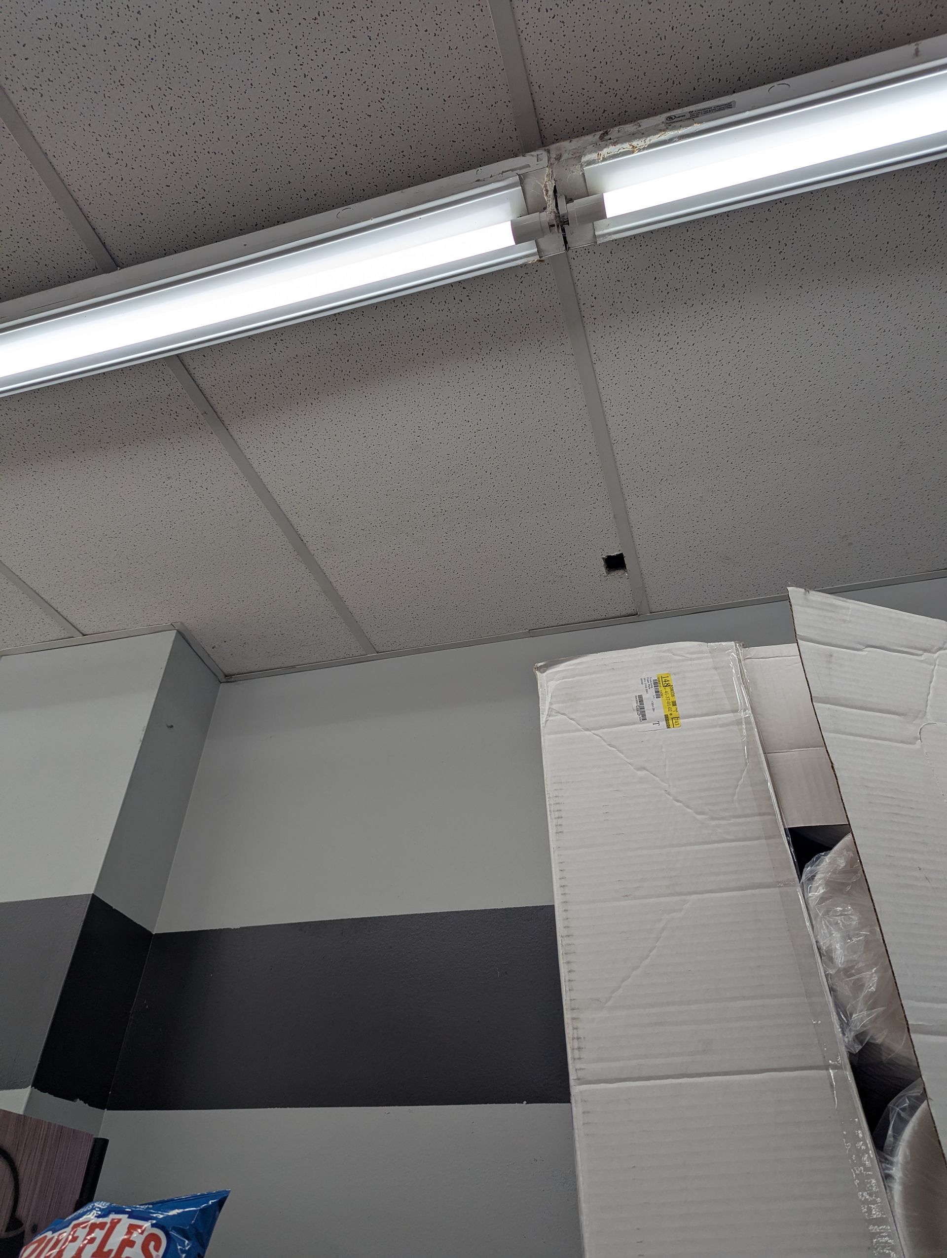 Fluorescent lights attached to a speckled drop ceiling above a cardboard shipping box.