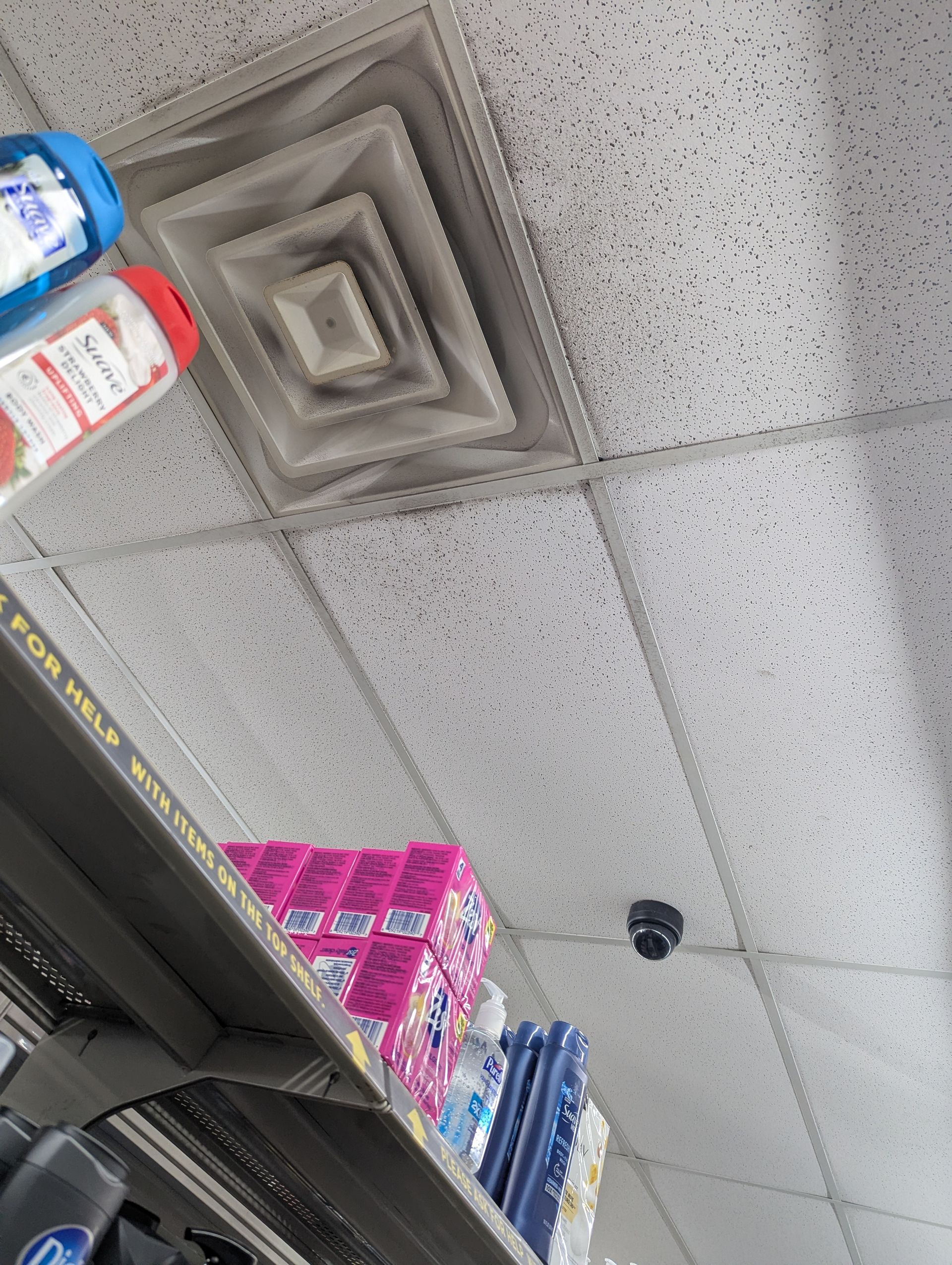 A ceiling vent with visible dust buildup above retail shelves stocked with various products.