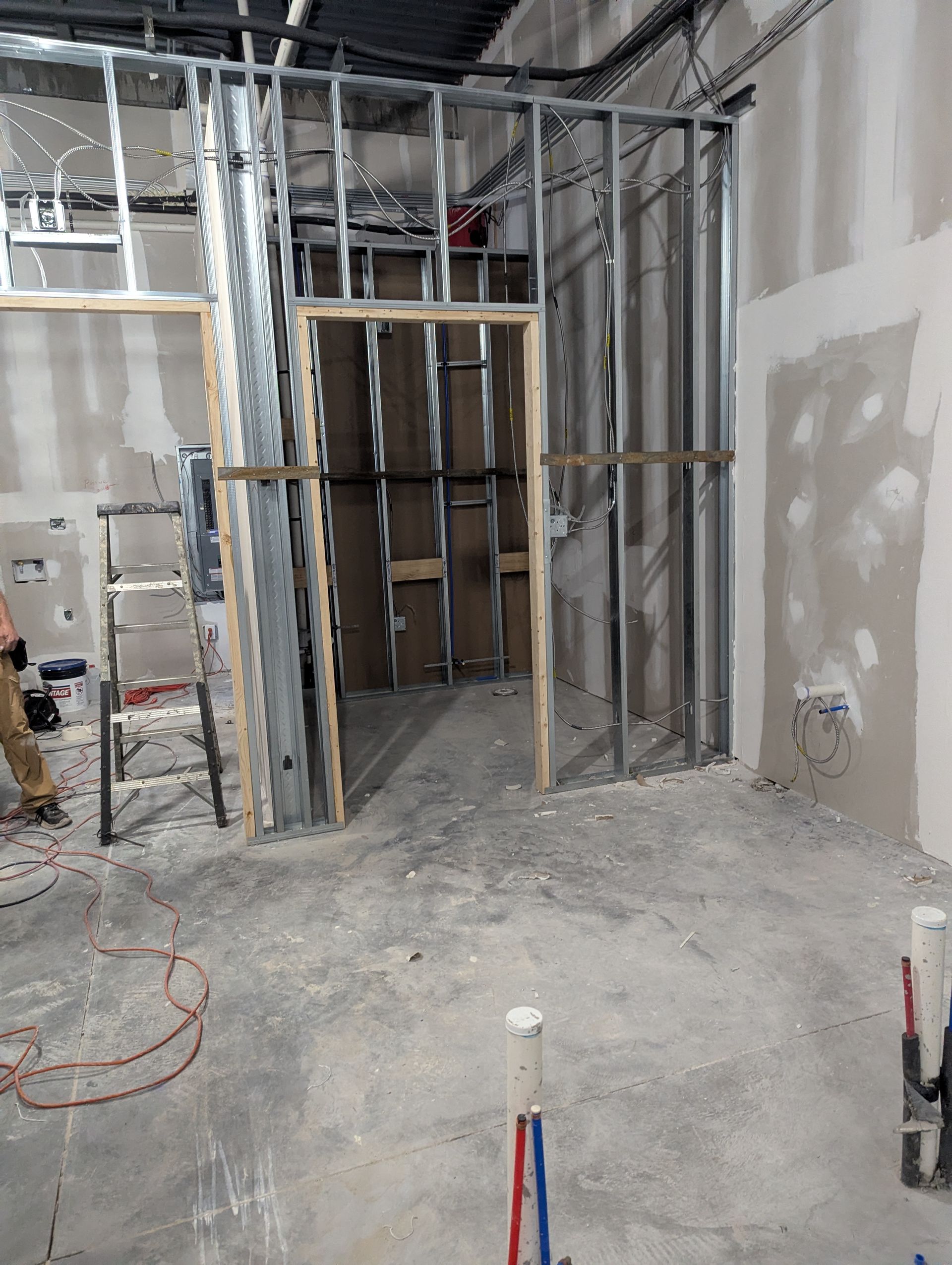 Interior view of a room under construction with metal wall studs, an unfinished doorway, and exposed wiring.