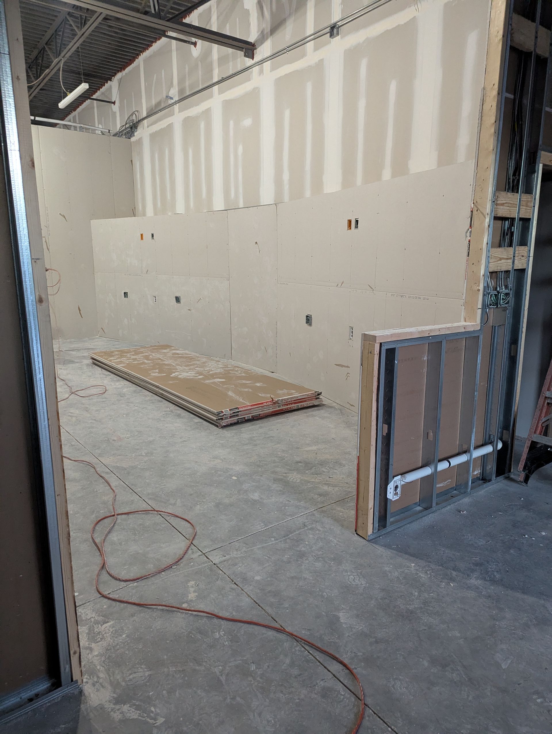 Interior of a construction site with partially installed drywall, exposed metal framing, and an electrical wire on the floor.