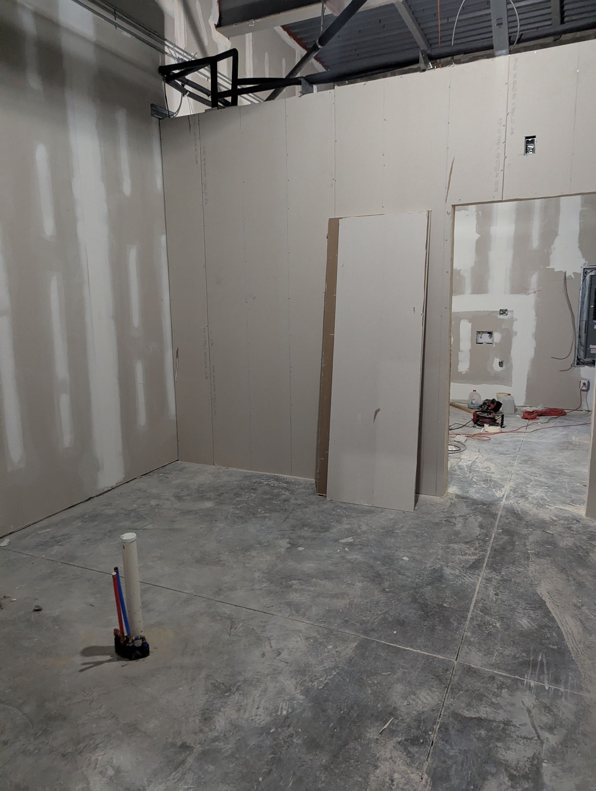 Construction interior with unpainted drywall walls, a doorway opening, and a pipe protruding from the concrete floor.