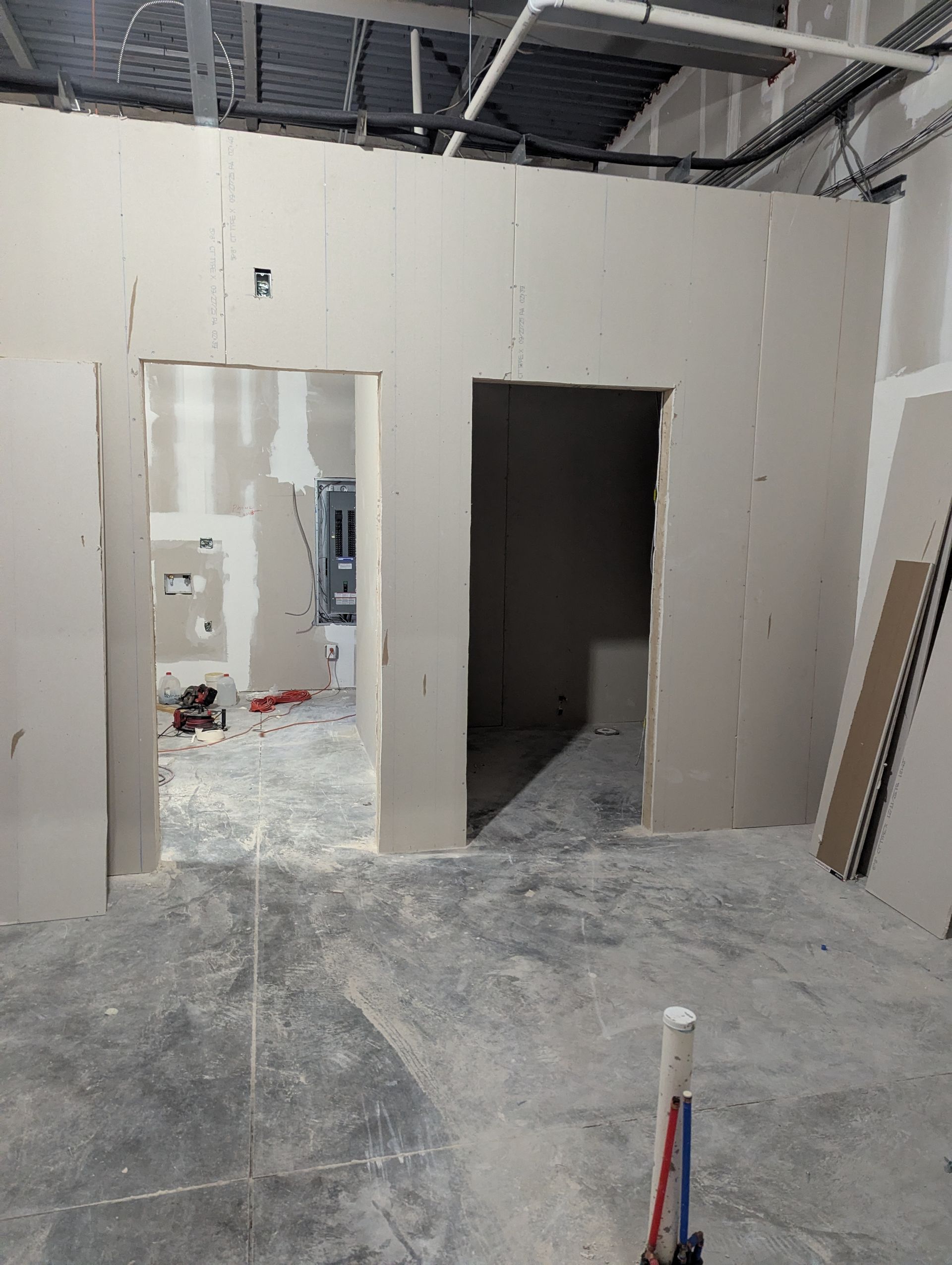 Interior view of a construction site showing two doorways framed in newly installed drywall, with exposed floor and wiring.