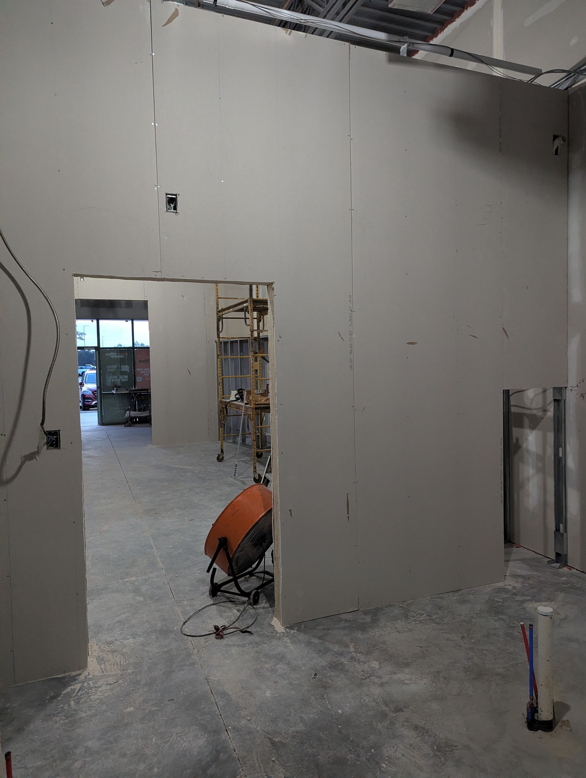 A room under construction with unfinished drywall, a doorway looking into another space, a scaffolding tower, and a fan.