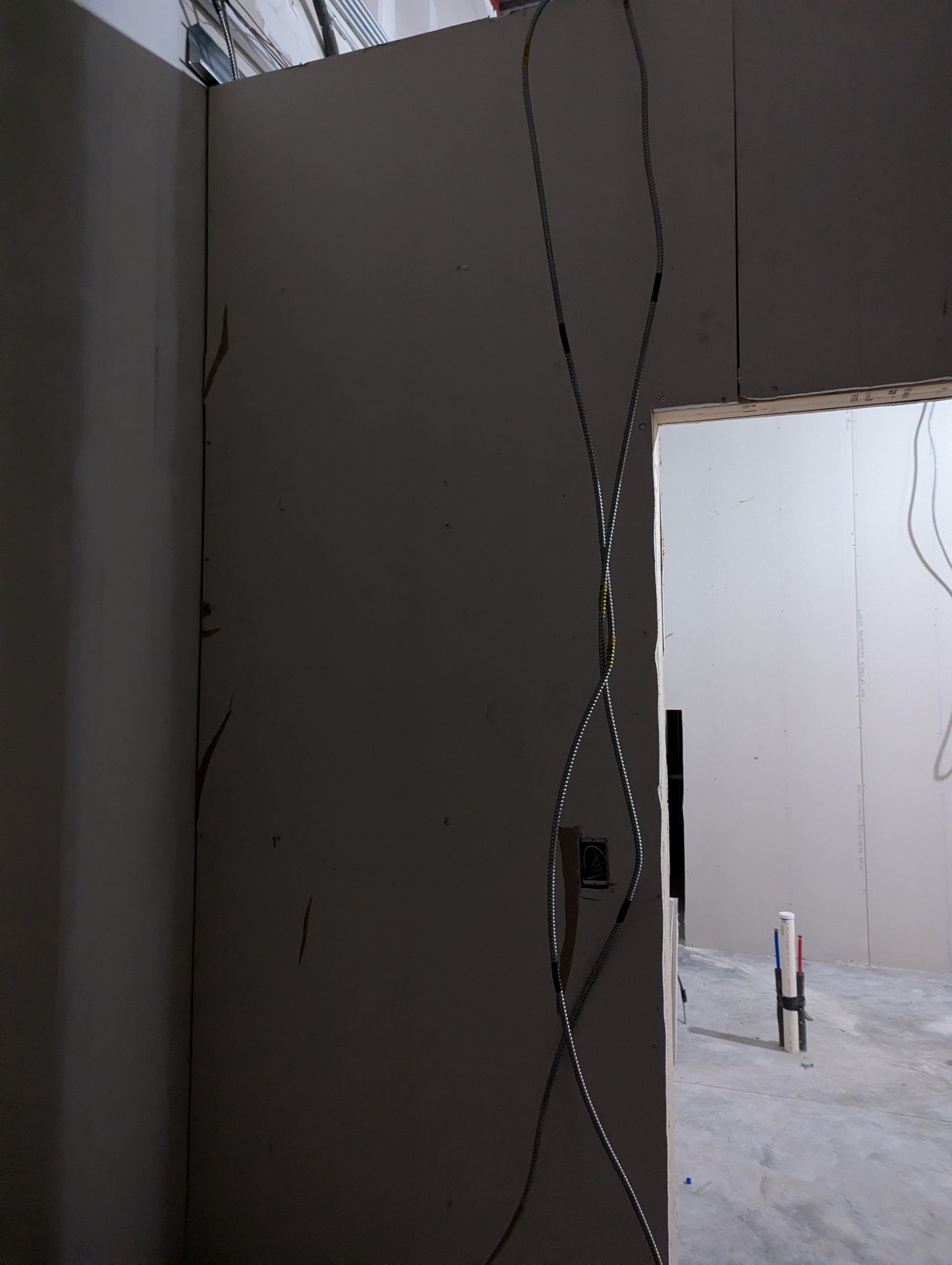 A vertical crack runs through a drywall panel next to a doorway in an unfinished room.