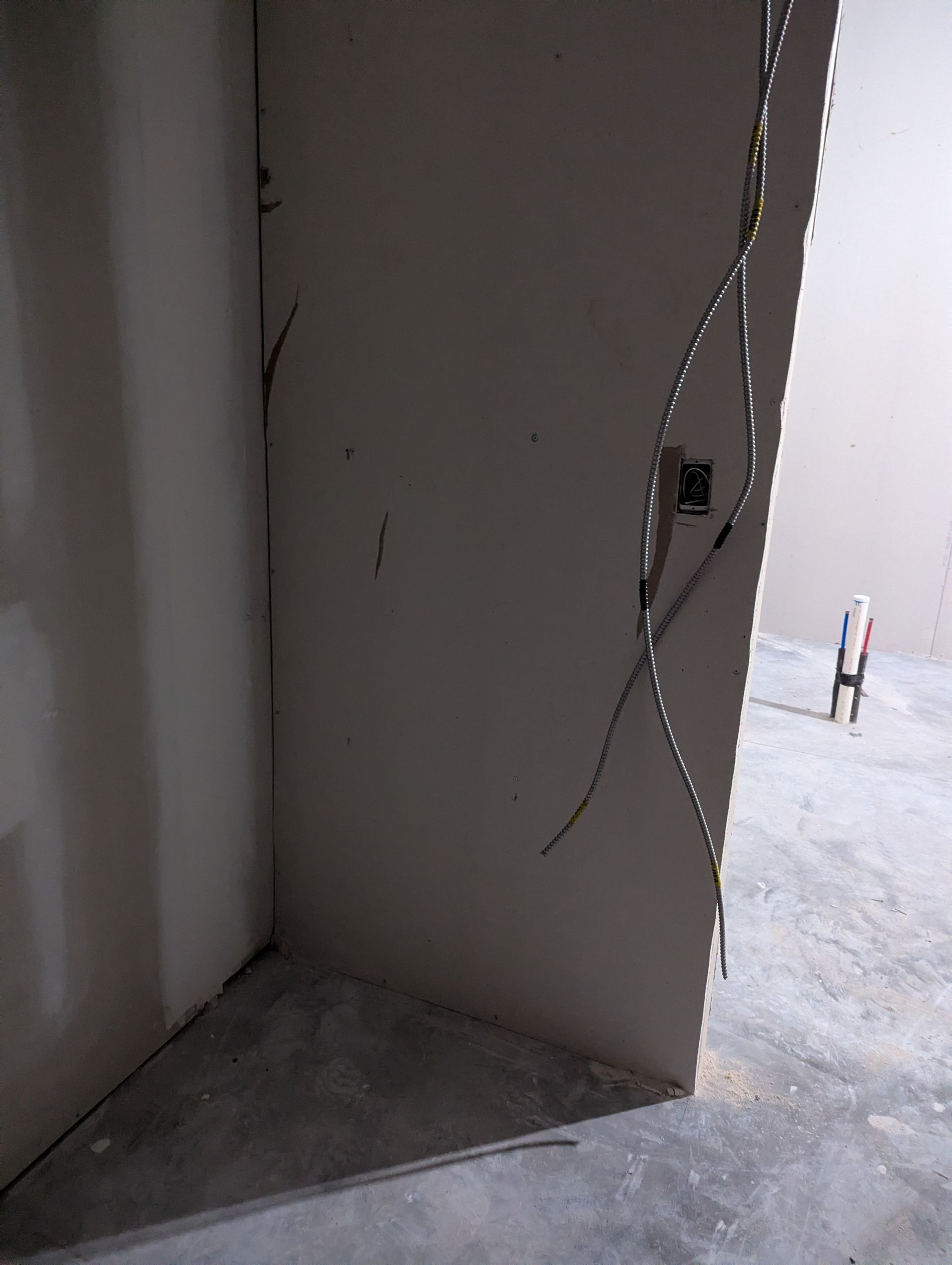 A partially constructed room with unpainted drywall walls and a metallic, spiraling piece of trim or stud on the corner.