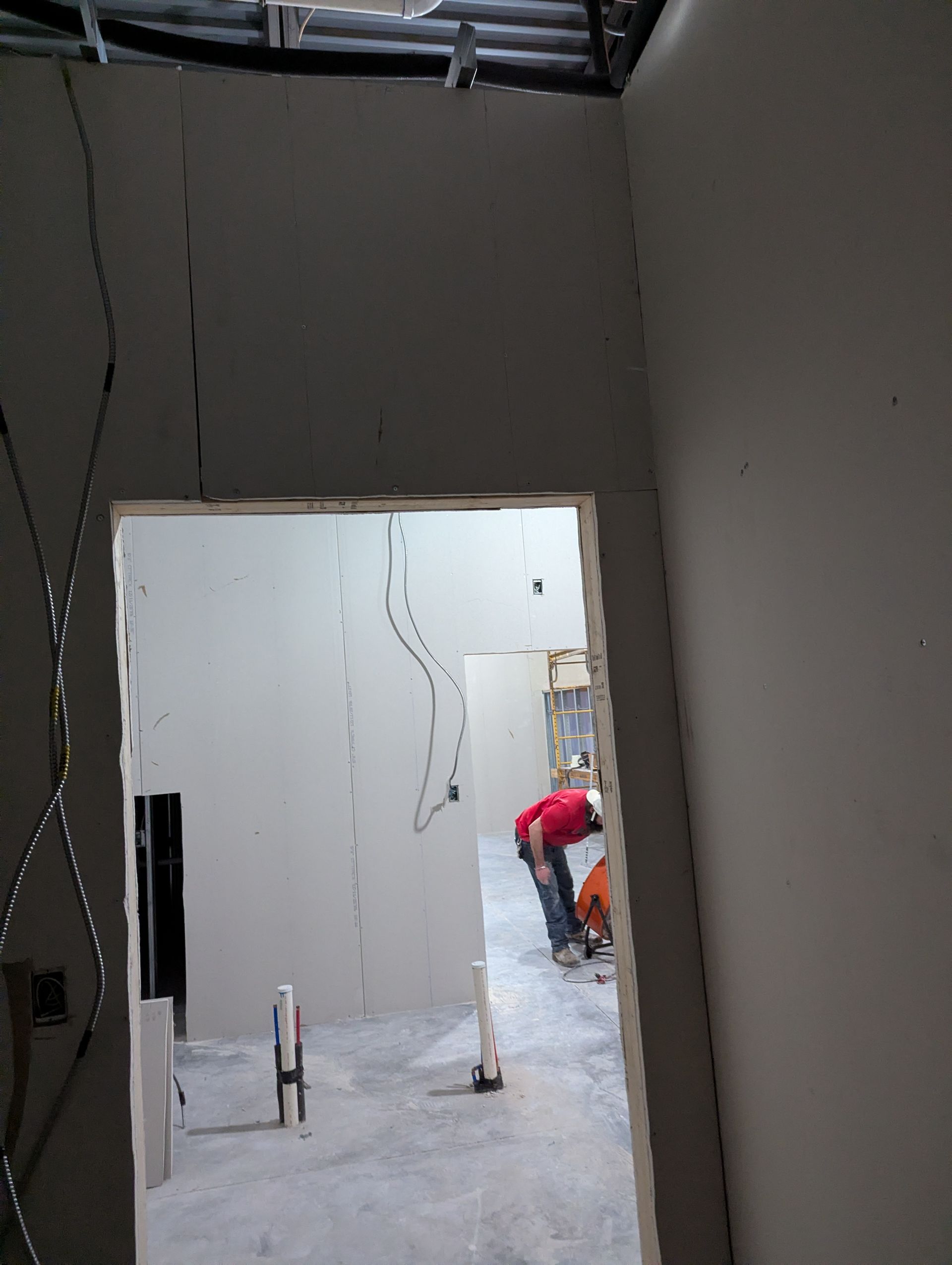 Interior view through a doorway into a room under construction with drywall, exposed wiring, and a person working.