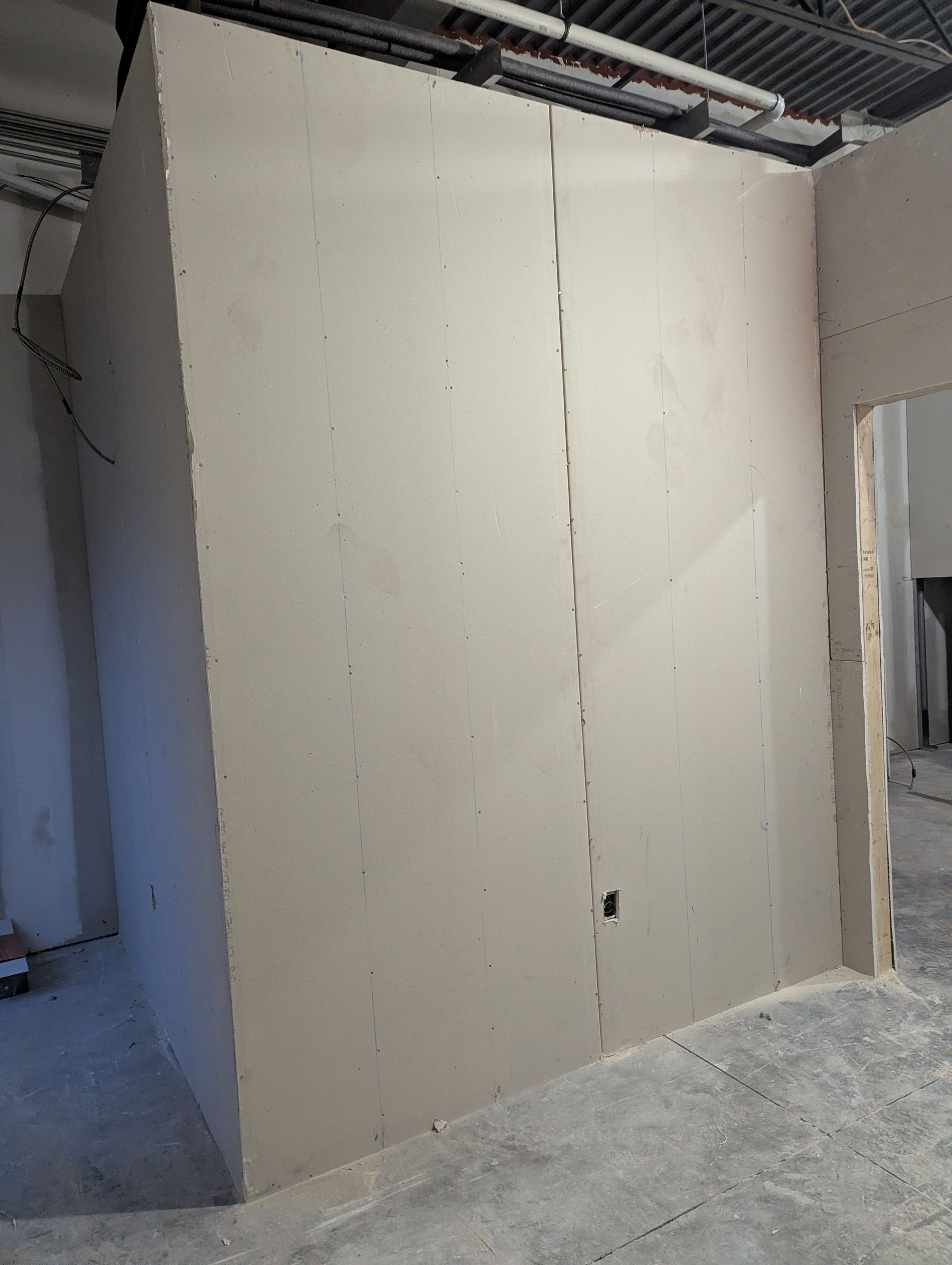Unfinished construction wall featuring two large gray drywall panels meeting at a seam in a room with a concrete floor.