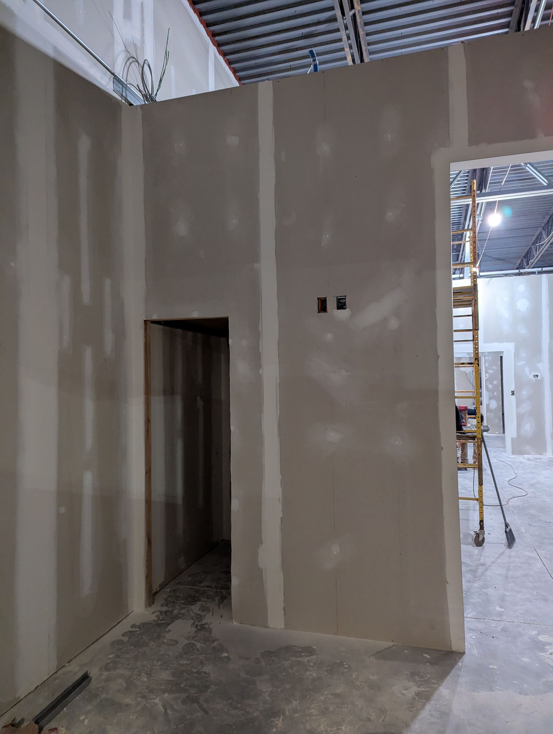 Interior view of unfinished drywall walls, a doorway, and a metal ladder visible through an open frame.