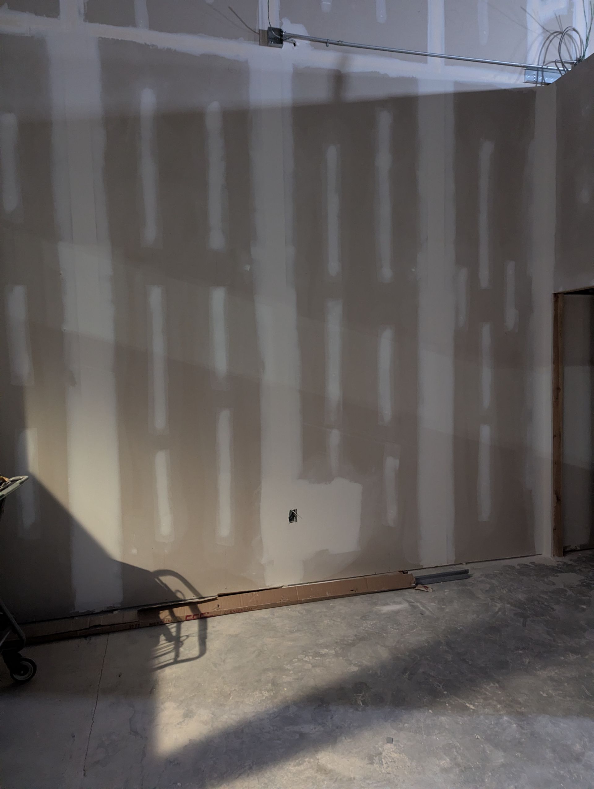 A wall under construction with unfinished drywall, tape over seams, and visible electrical outlets in a room.