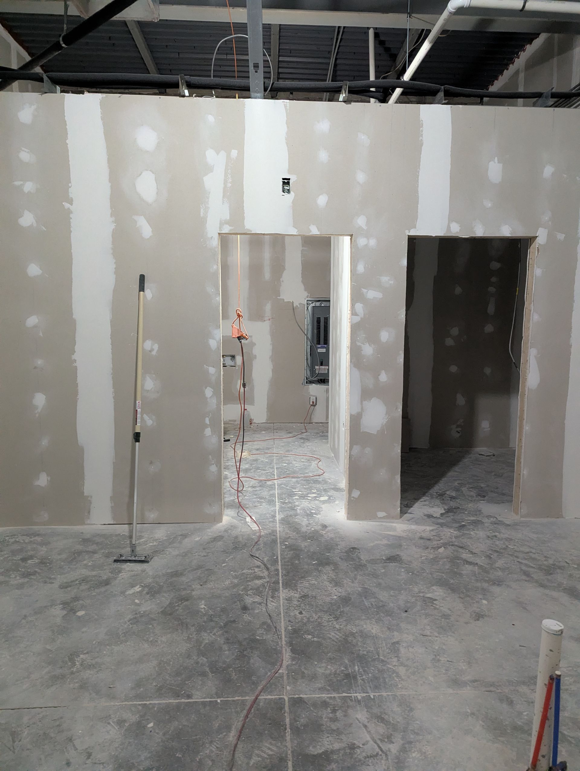 An unfinished room with newly installed drywall, visible tape and spackle, and two doorways leading into a dark interior.
