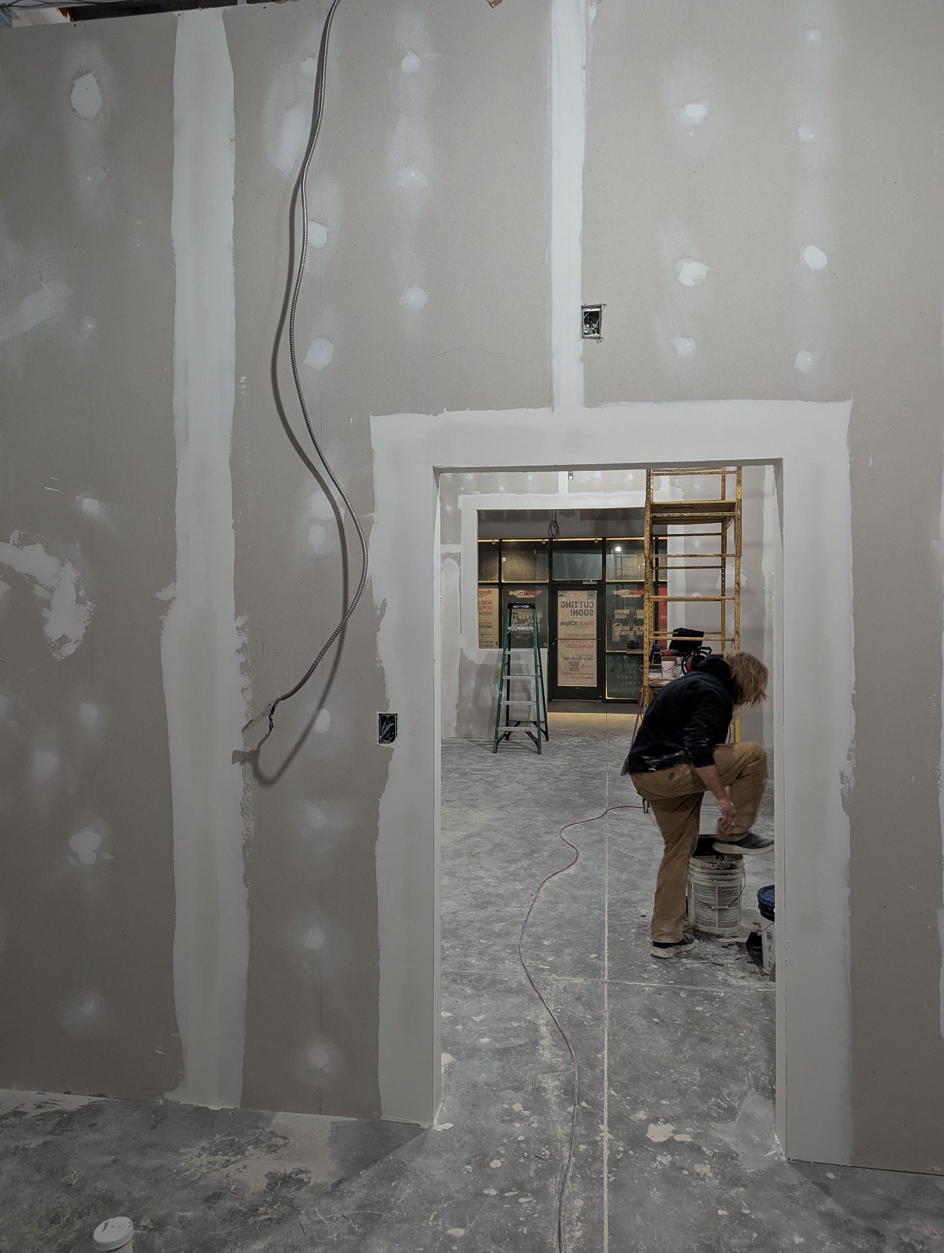 A person working in a doorway of a room under construction with unfinished drywall, plaster, and exposed wiring.