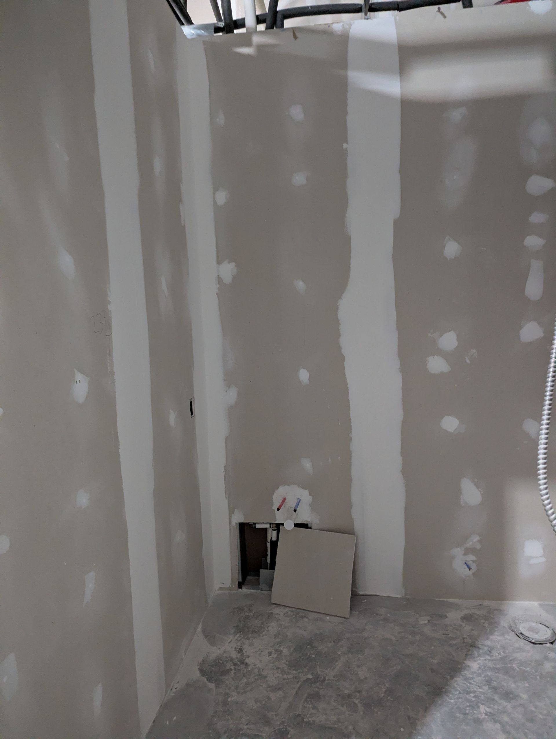 An unfinished room interior with taped drywall seams, a hole in the bottom wall, and construction debris on the floor.