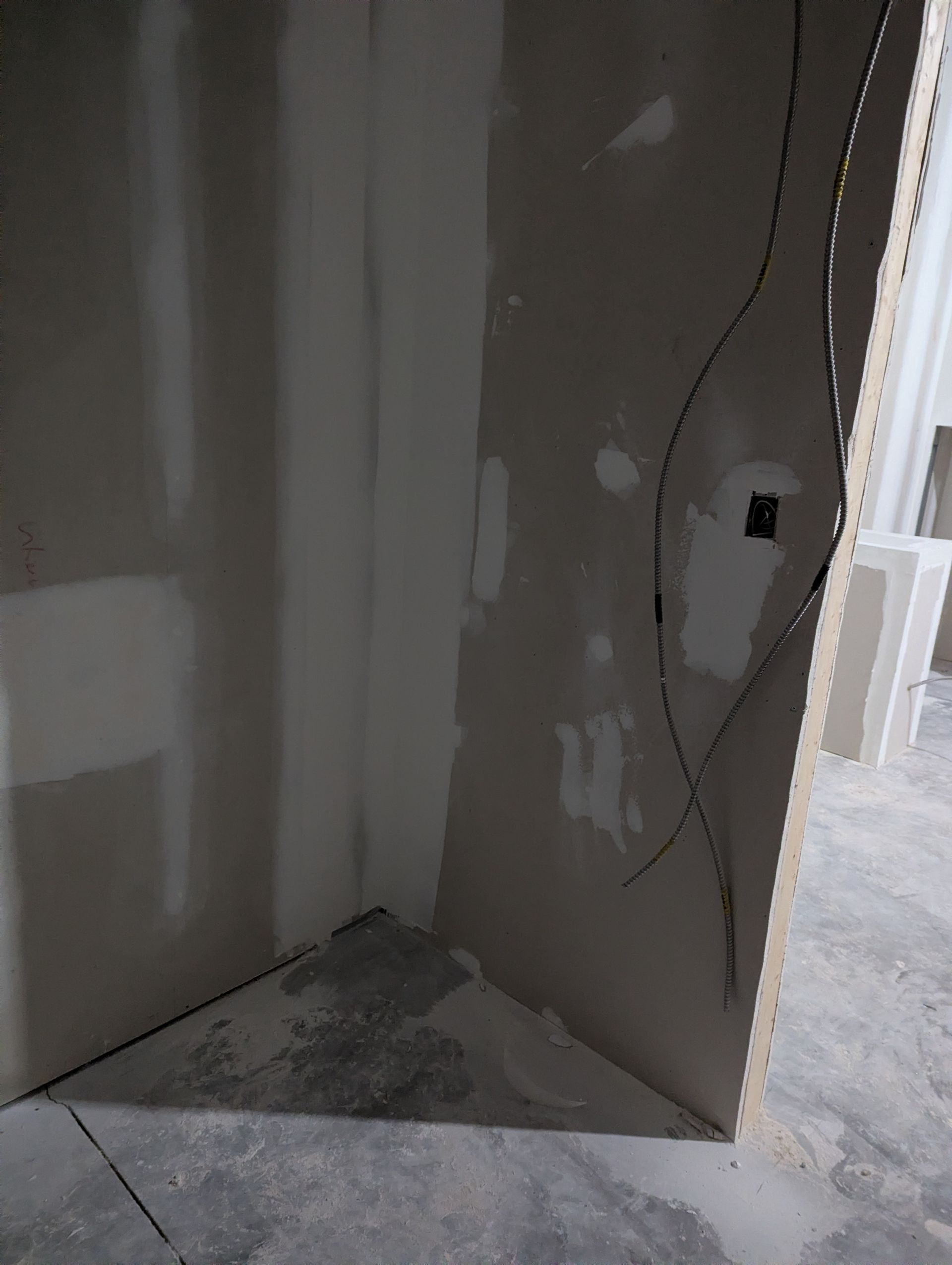 Unfinished drywall corner under construction with exposed wires hanging against the wall.