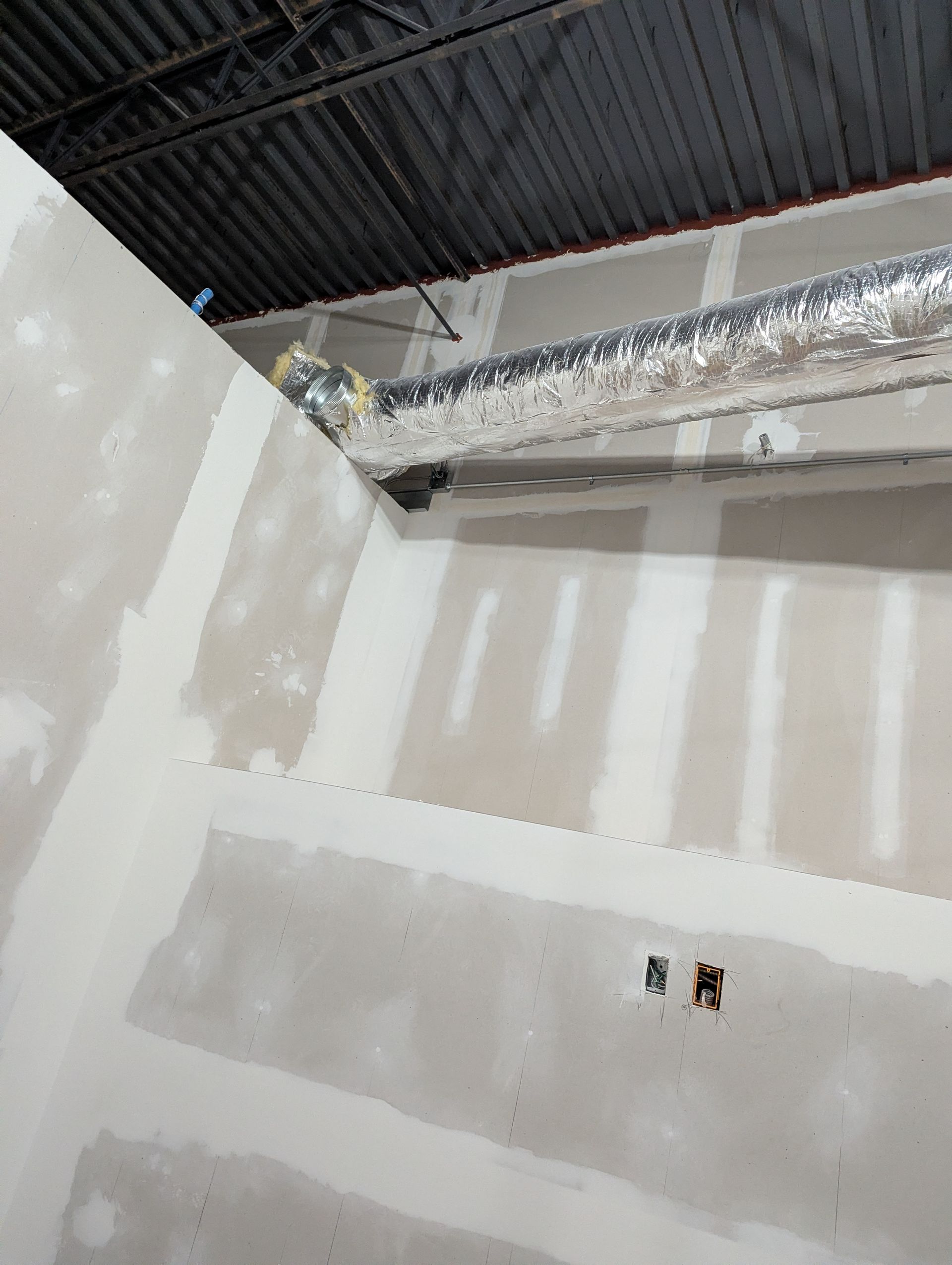 Unfinished drywall interior with taped seams, an exposed ceiling, and an insulated HVAC duct.