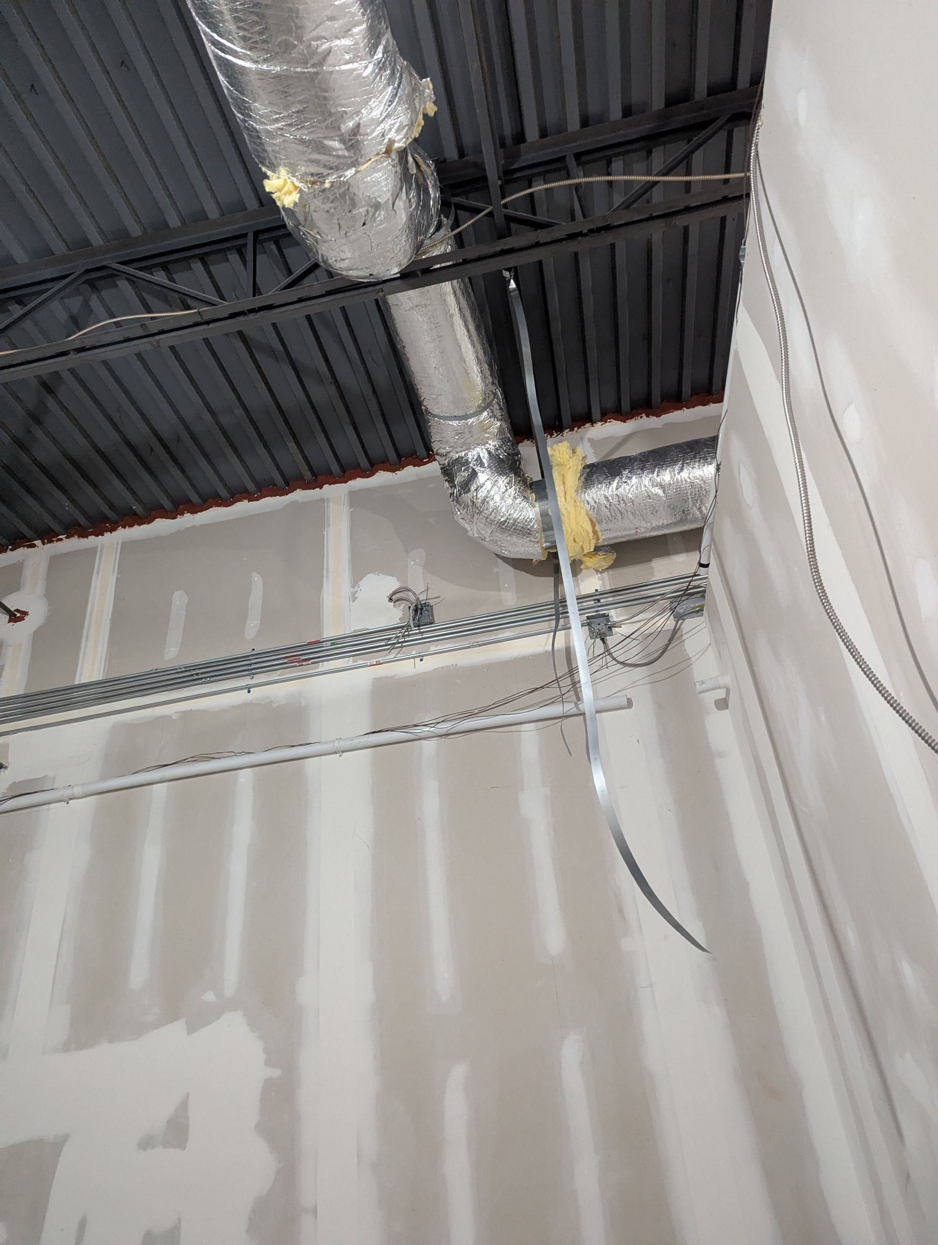 Unfinished interior room with exposed ceiling rafters, silver ductwork, and partially installed drywall panels.