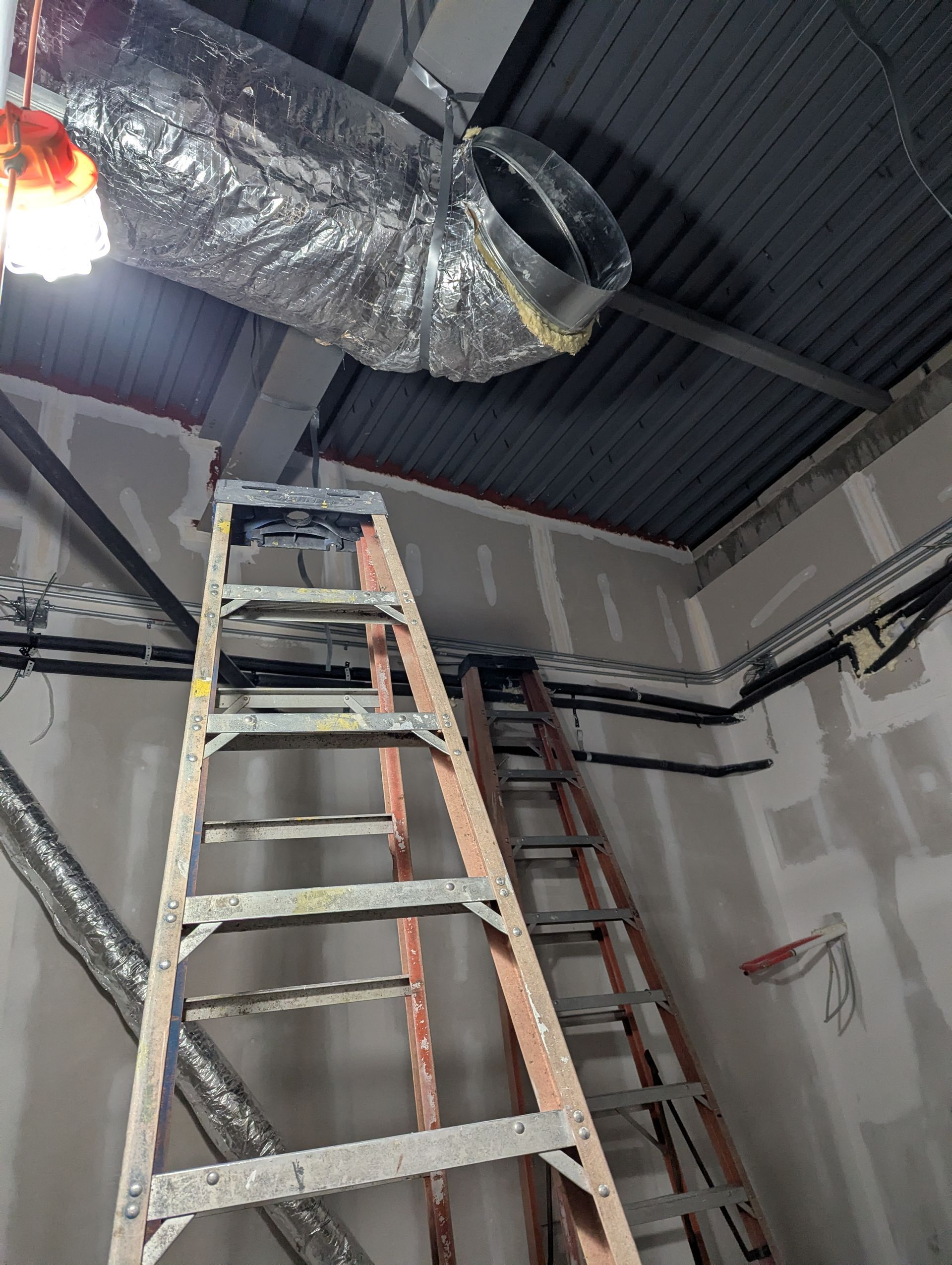 Two ladders positioned in a room with unfinished drywall and exposed ceiling ductwork.
