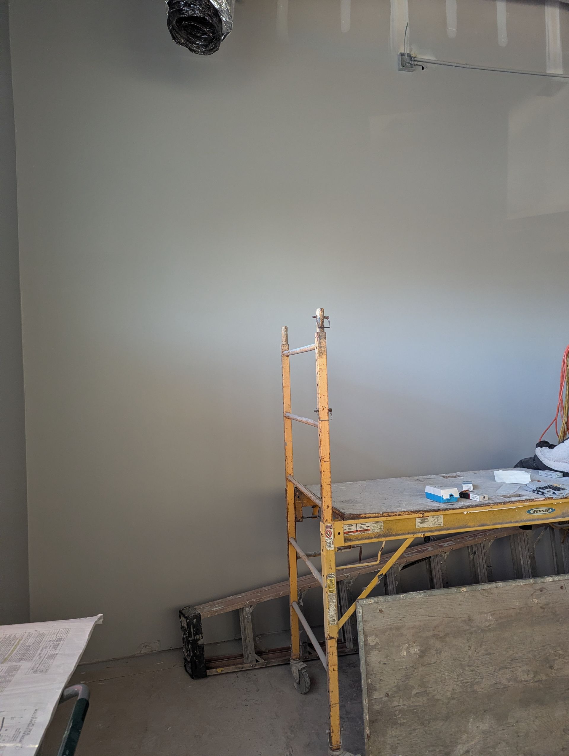 A gray painted wall in an unfinished room with yellow scaffolding standing in front of it.