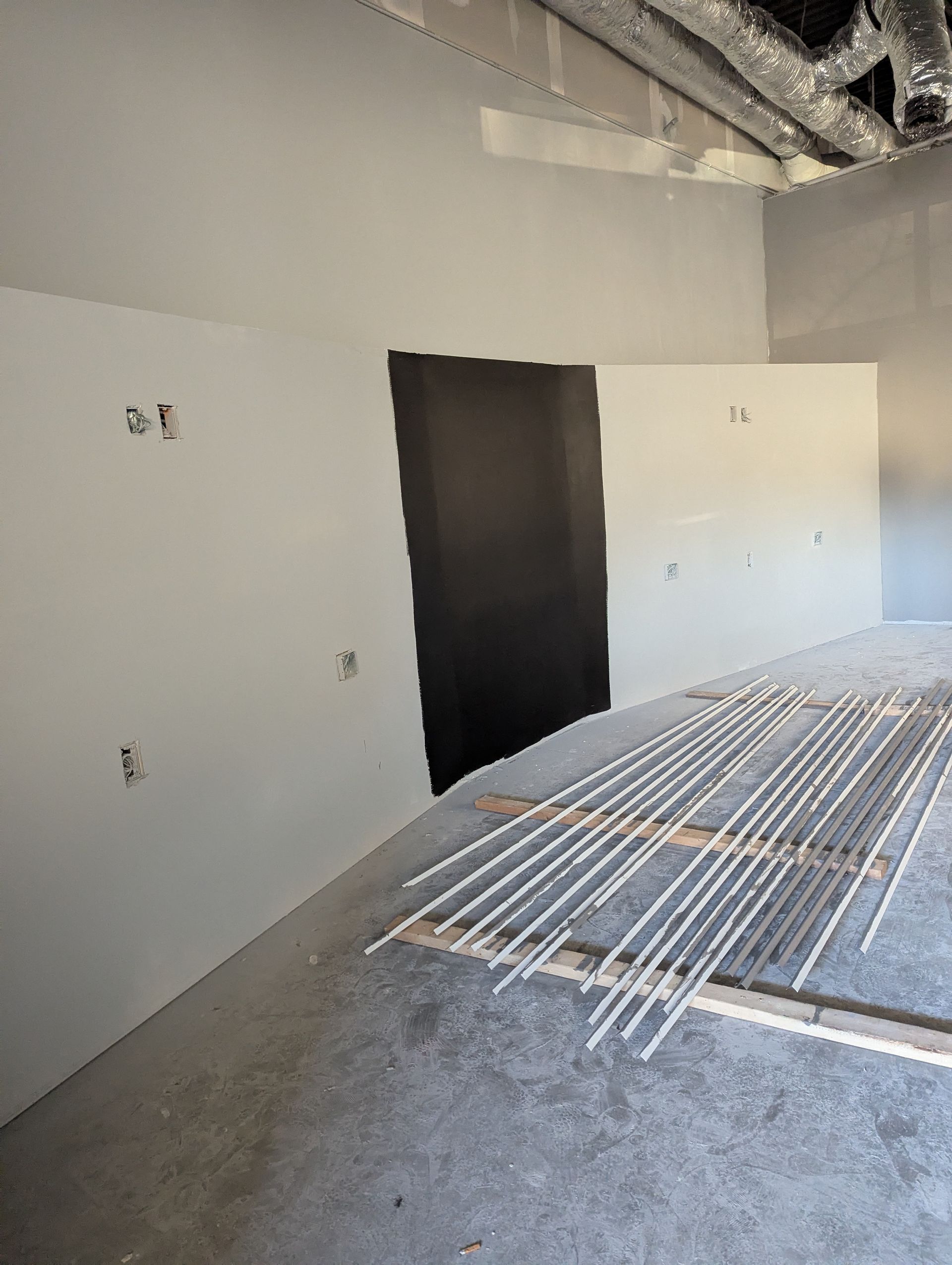 A construction site featuring a partially painted wall with white and black sections and scattered metal studs on the floor.