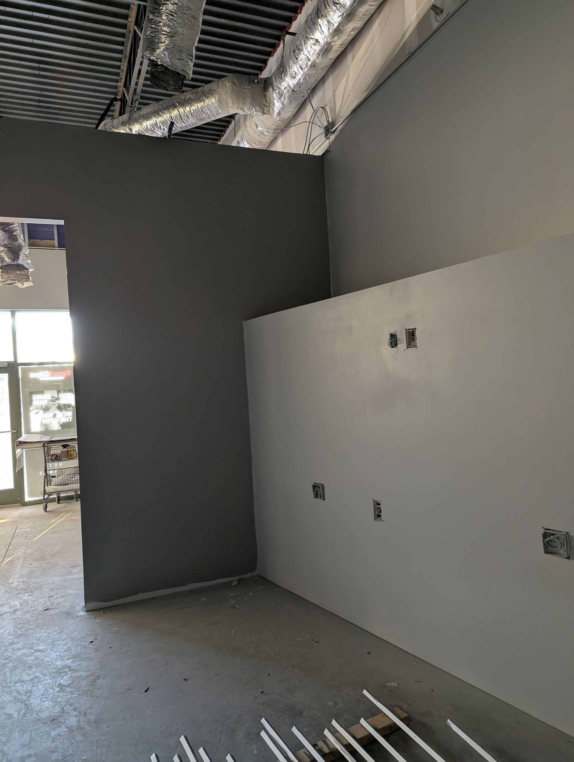 An interior view of a commercial space with a grey wall and an adjacent white wall featuring exposed electrical outlets.
