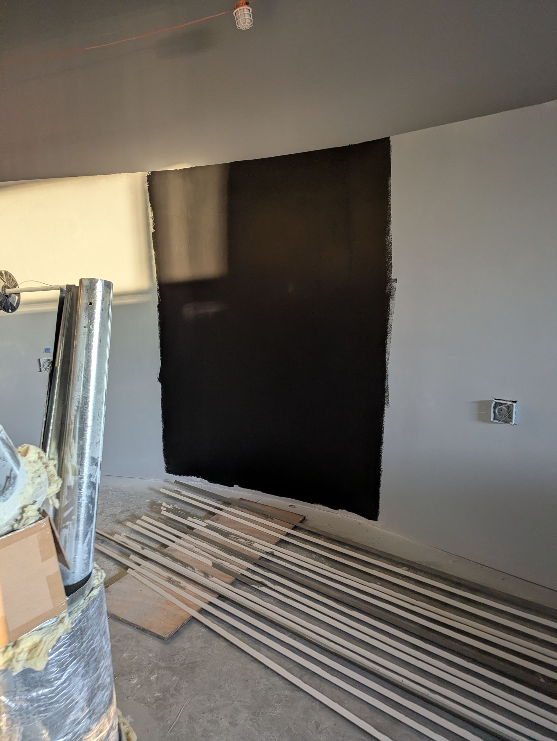 A large black rectangular patch painted on a light-colored wall in a room undergoing construction with metal studs.